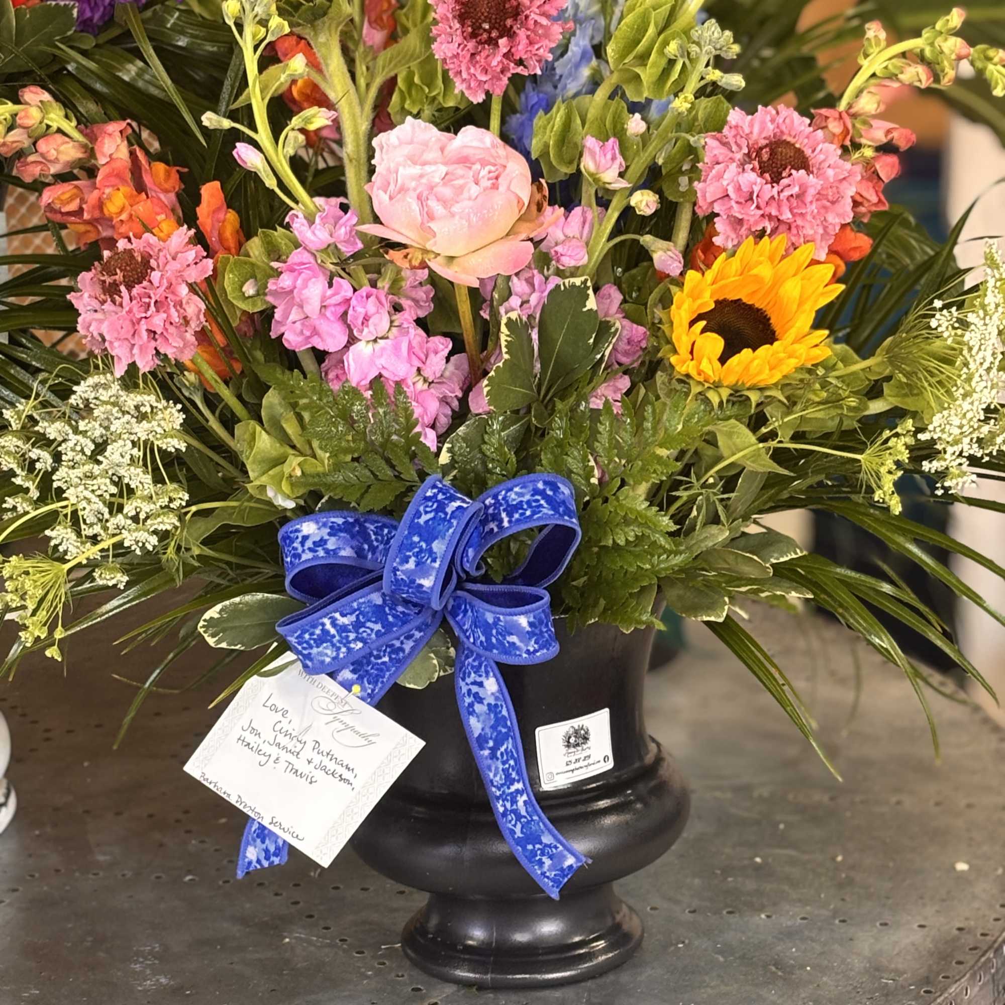 Bright, uplifted blooms in a black urn create a comforting yet celebratory