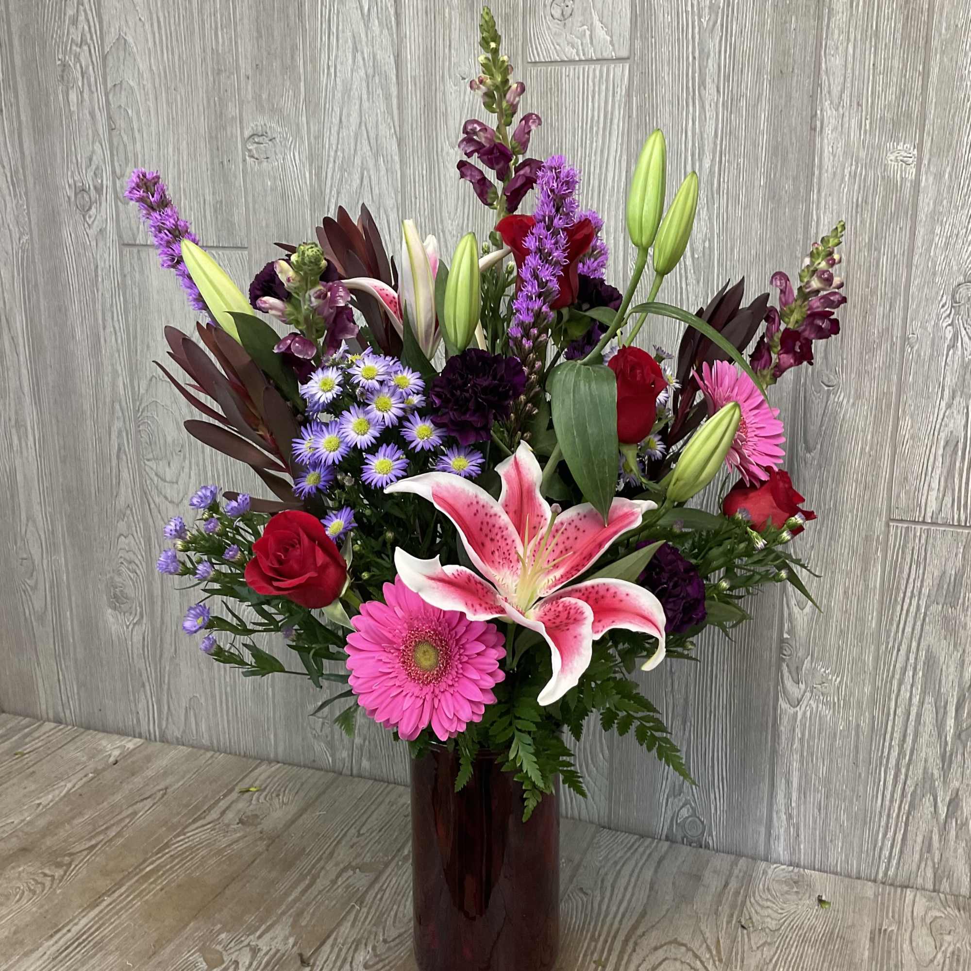 Mixed bouquet with lilies, roses, gerbera daisies, and purple filler in a tall vase