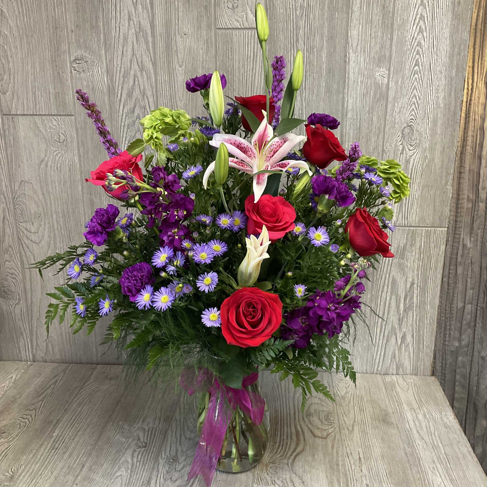 Mixed bouquet of red roses, lilies, and purple flowers in a glass vase