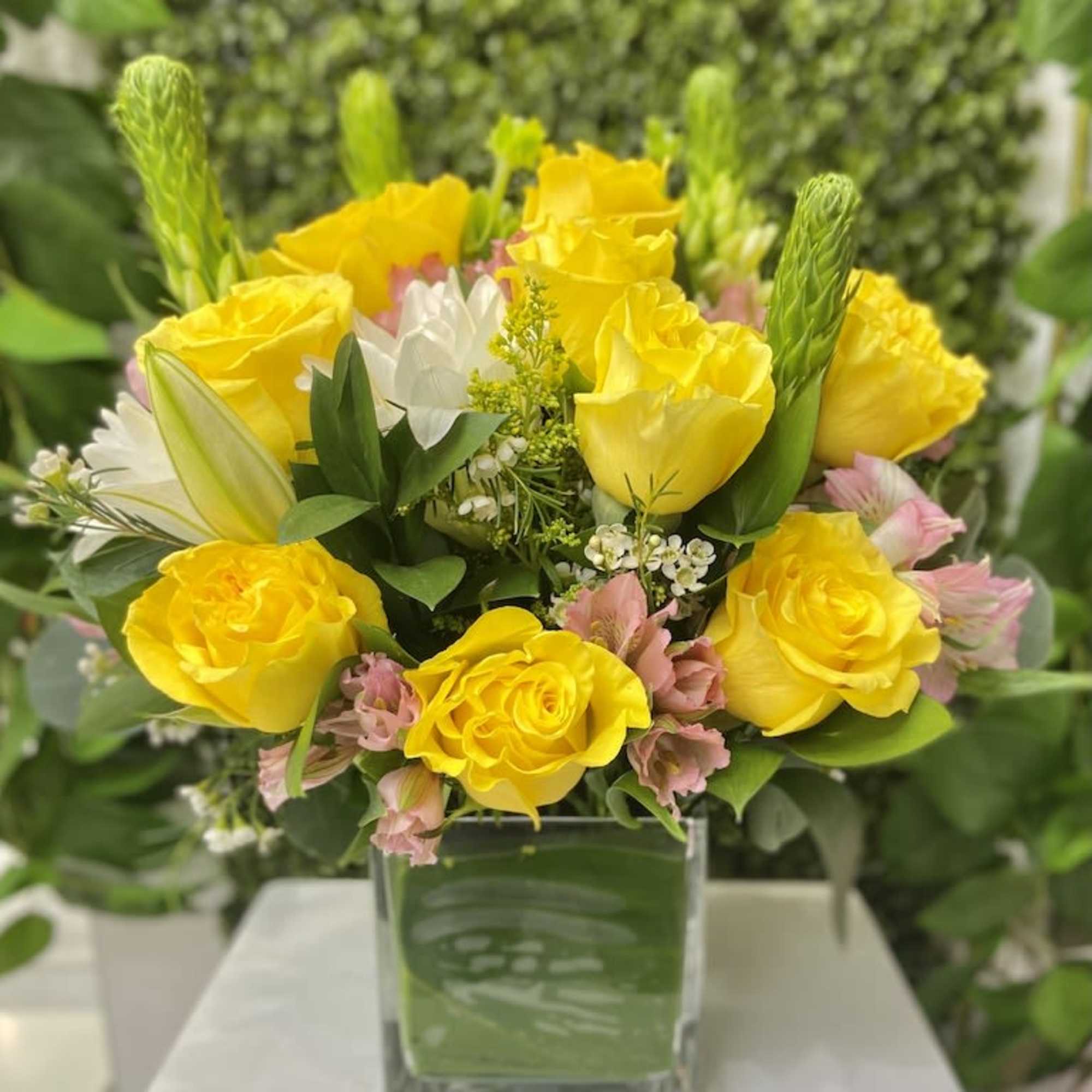 Yellow rose and mixed flower arrangement in a square glass vase with leaf lining