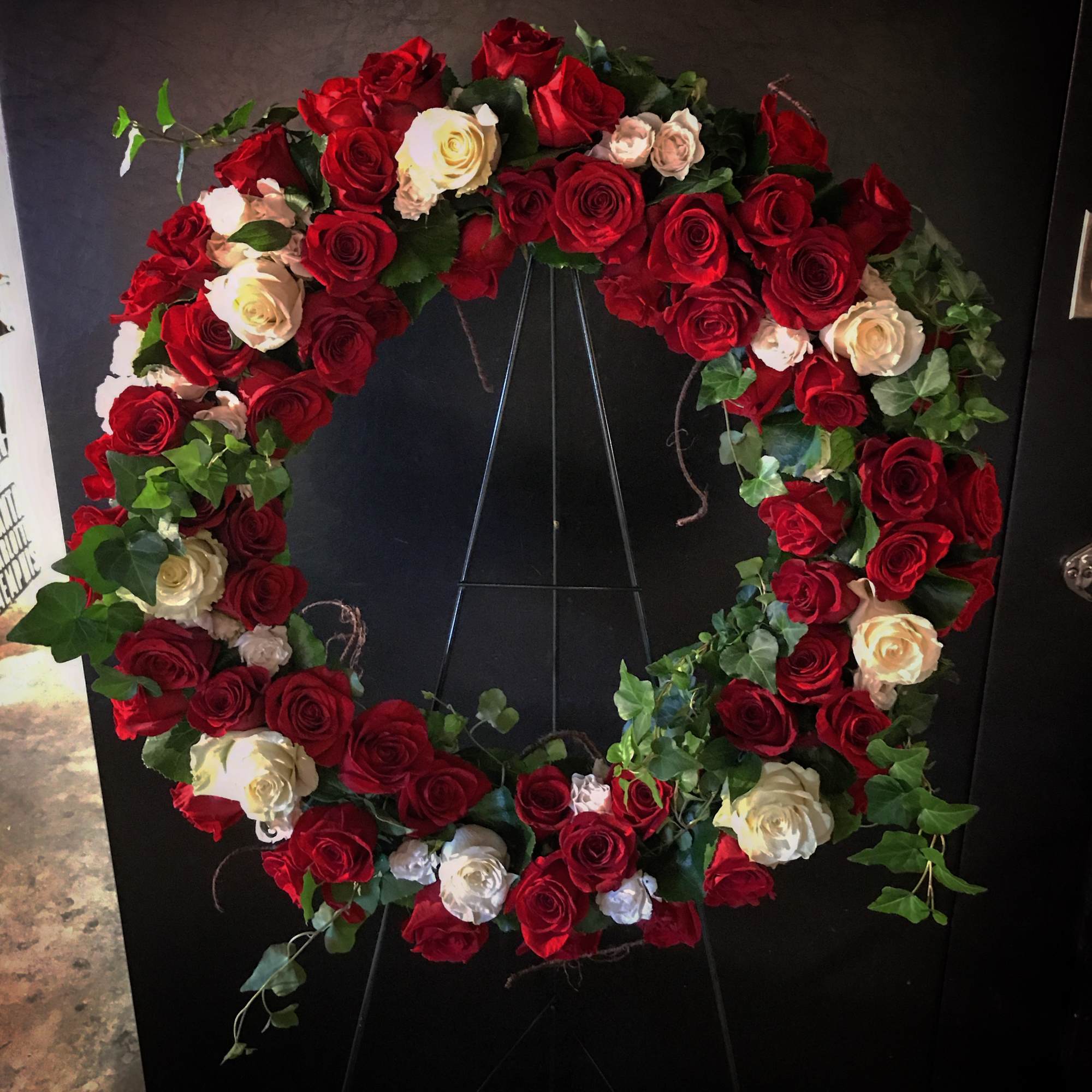 Circular wreath of red and white roses on a black stand