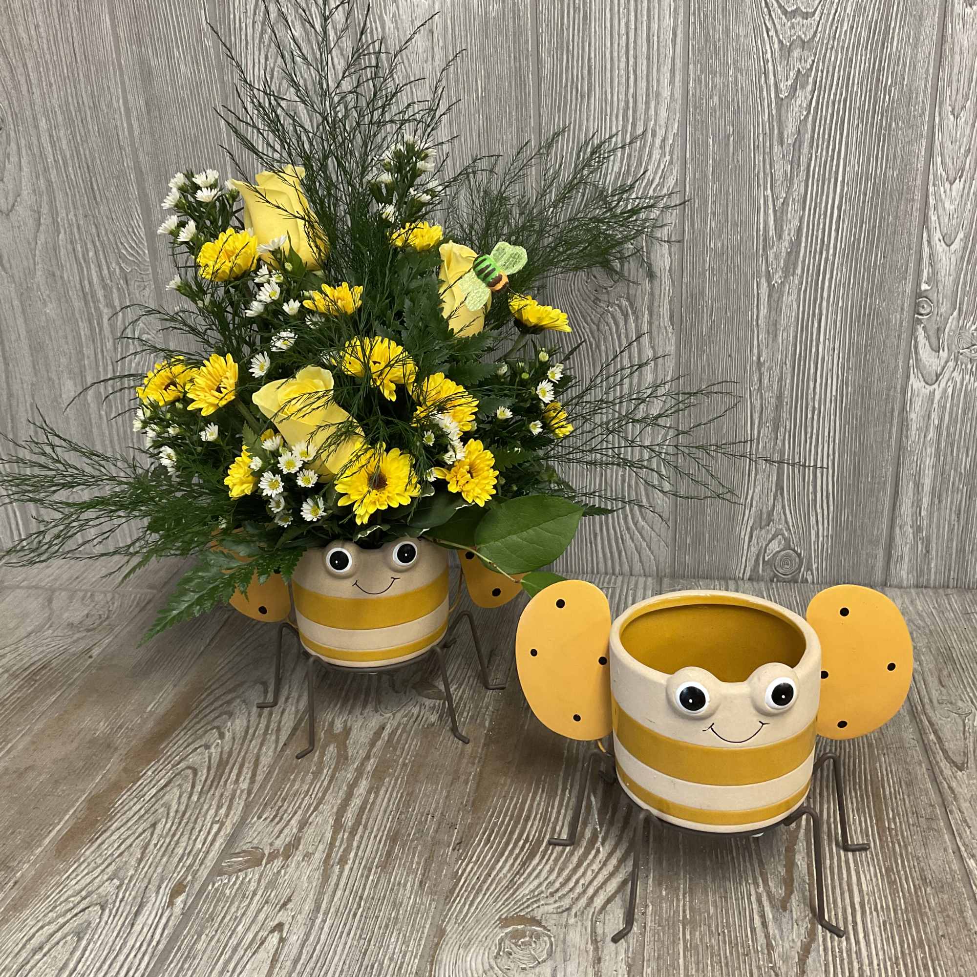 Yellow flower arrangement in a bee-shaped pot with a matching empty pot beside it.