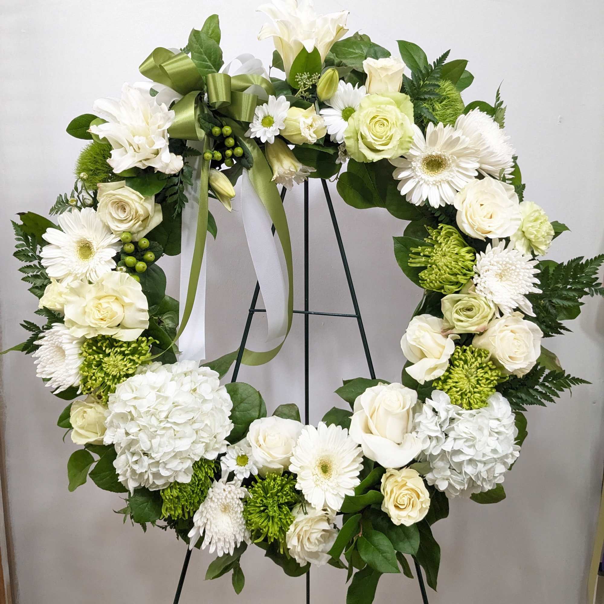 White floral wreath with roses, daisies, and hydrangeas on a stand