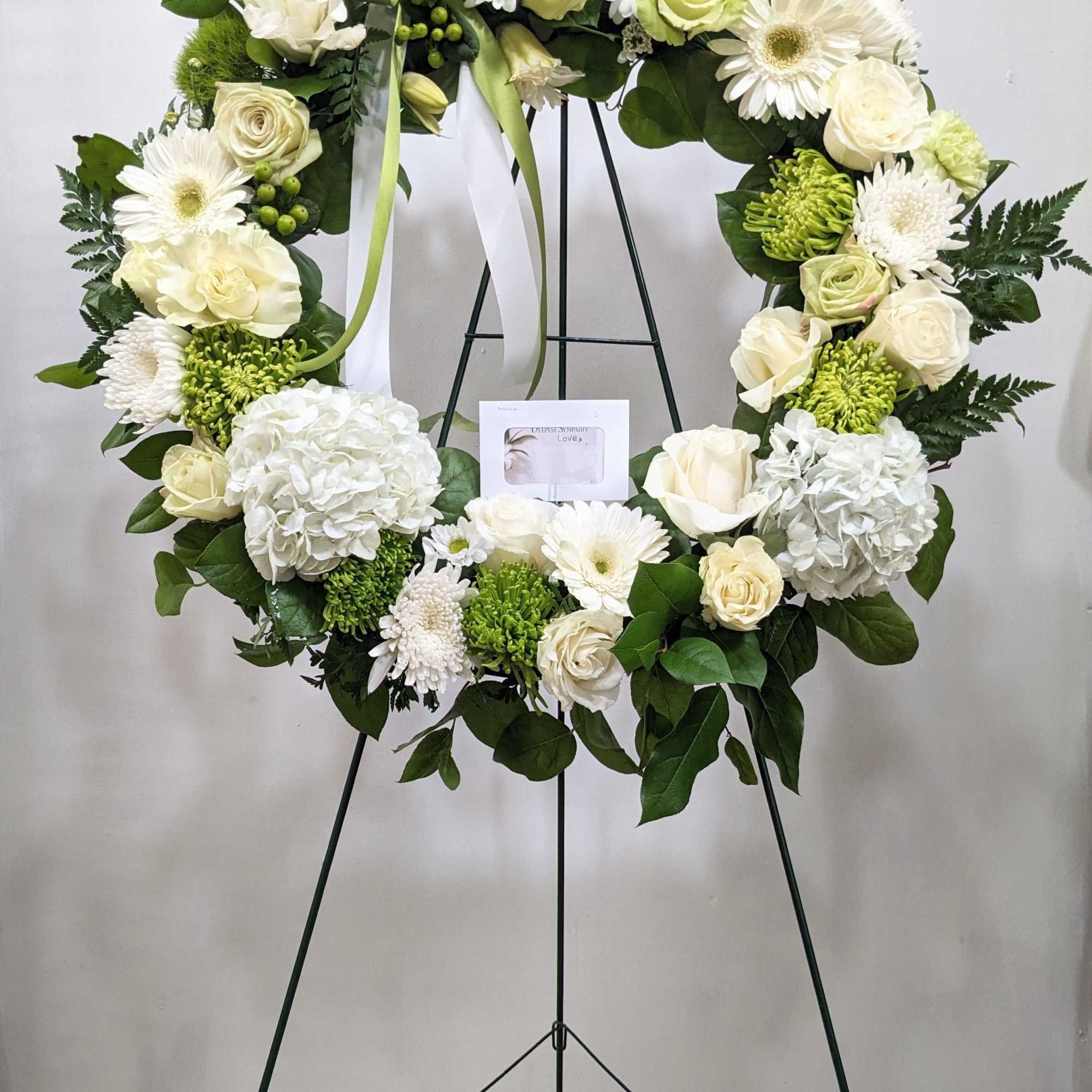 White and cream floral wreath on a black stand with green ribbon