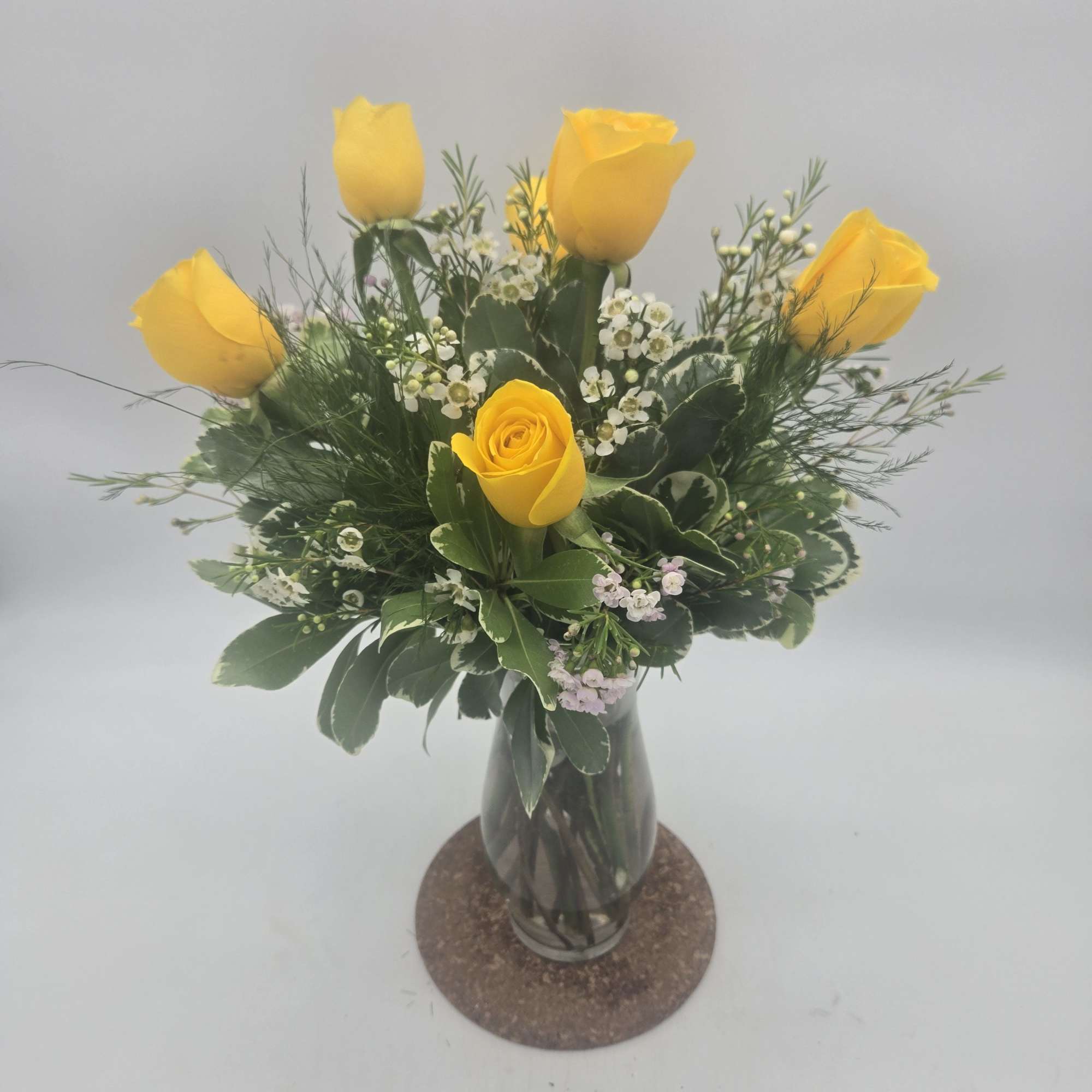 Yellow roses arranged in a glass vase with mixed greenery