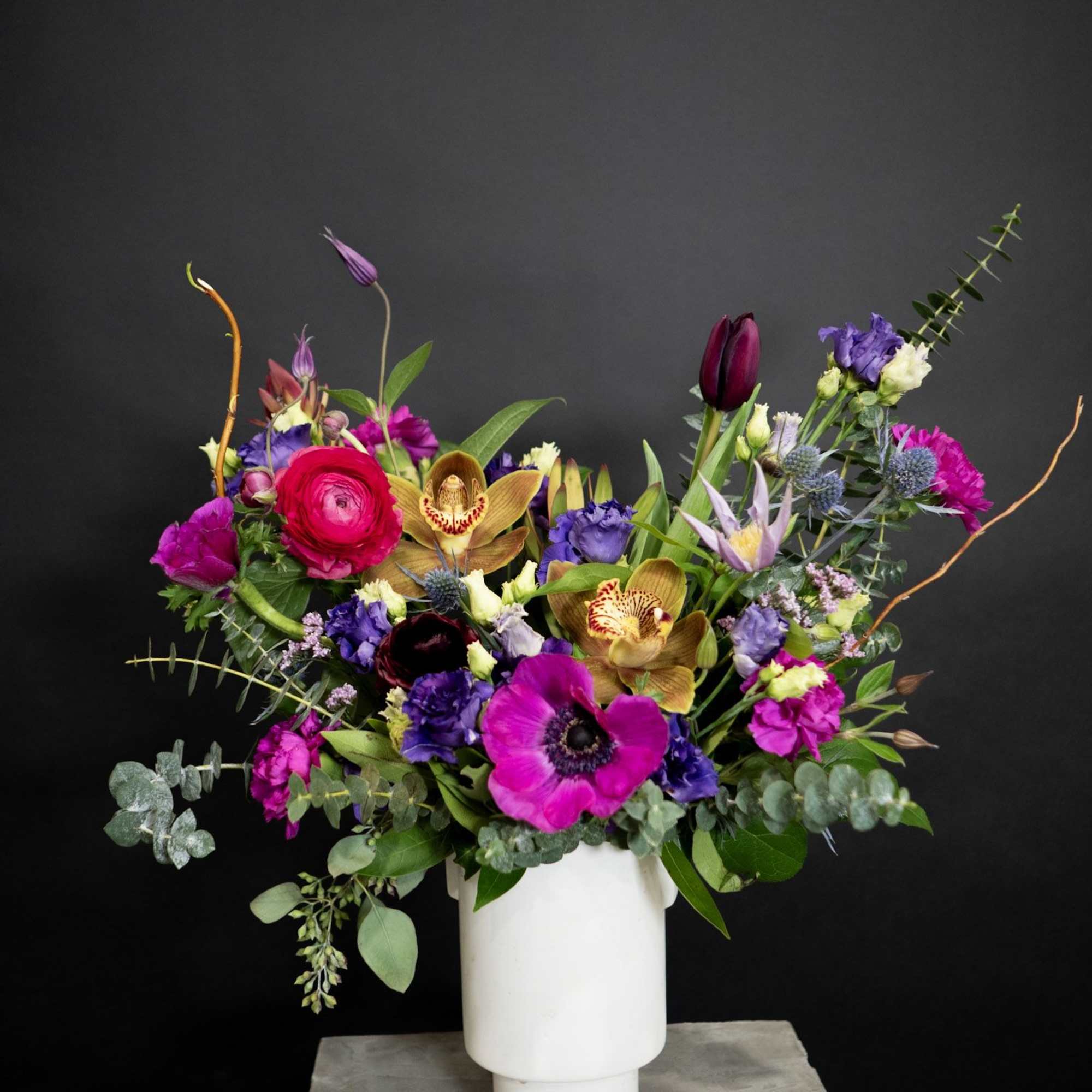 Colorful mixed bouquet in a white vase with orchids and anemones