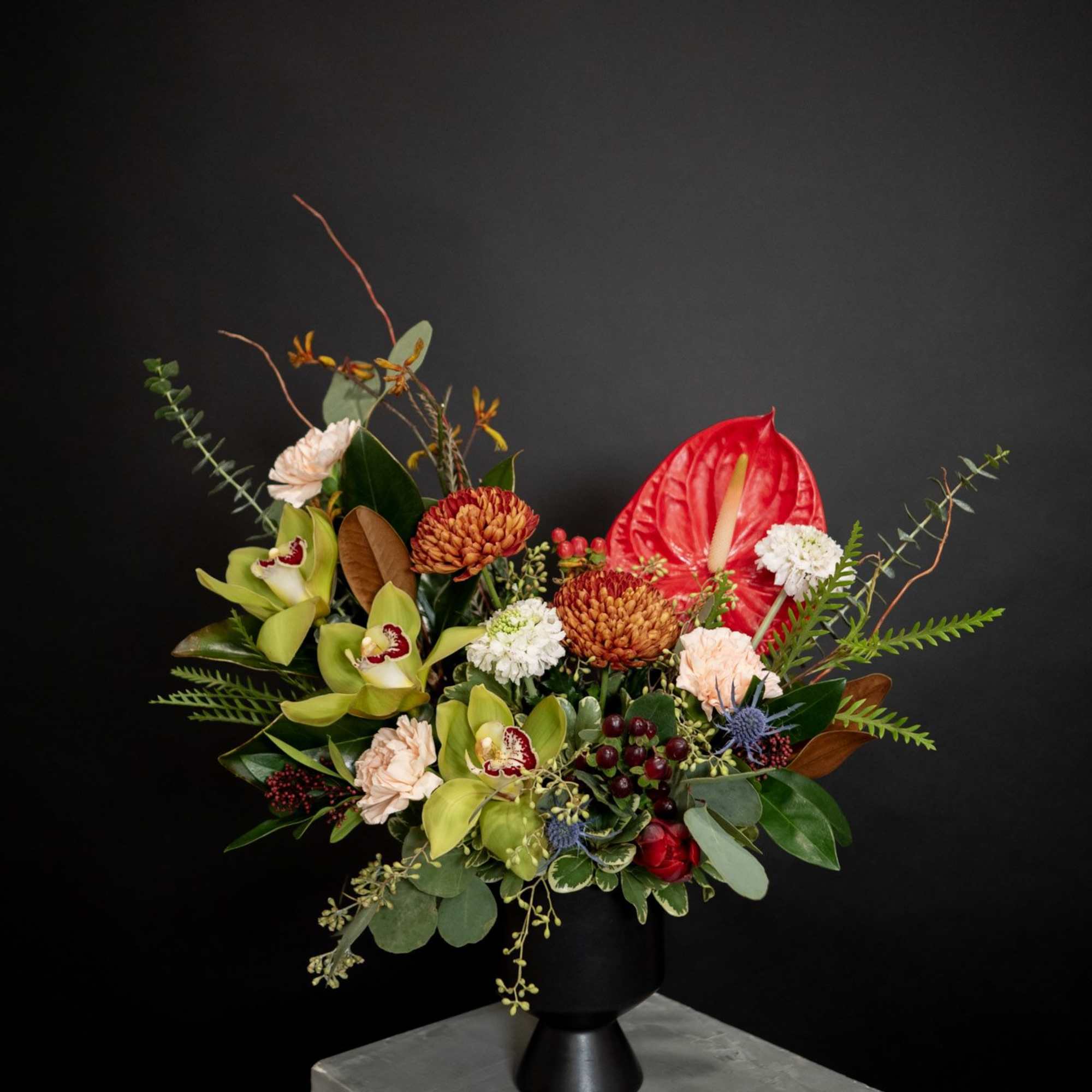 Mixed floral arrangement in a black vase with red anthurium and green orchids