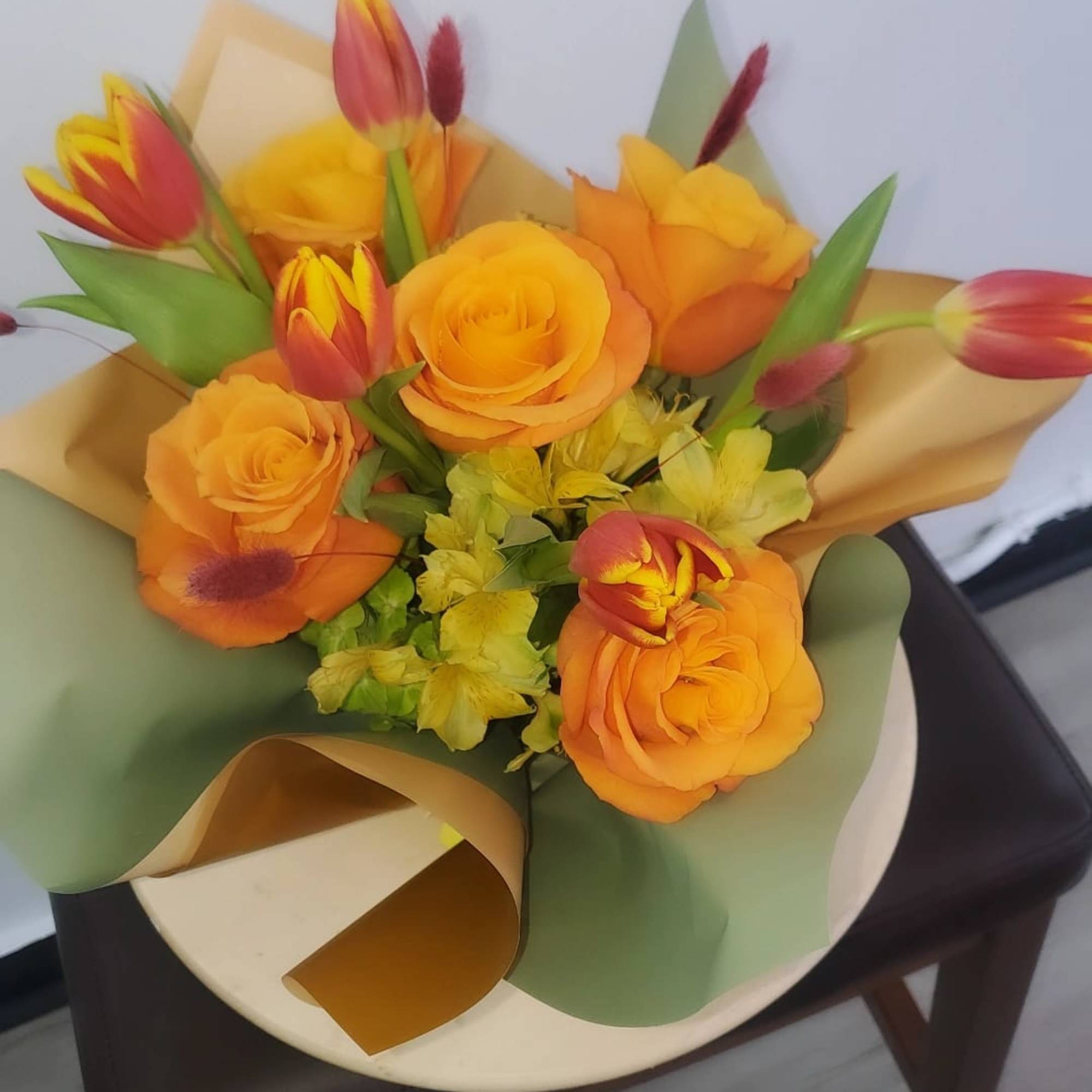 Bouquet of orange roses and red-yellow tulips wrapped in green and gold paper