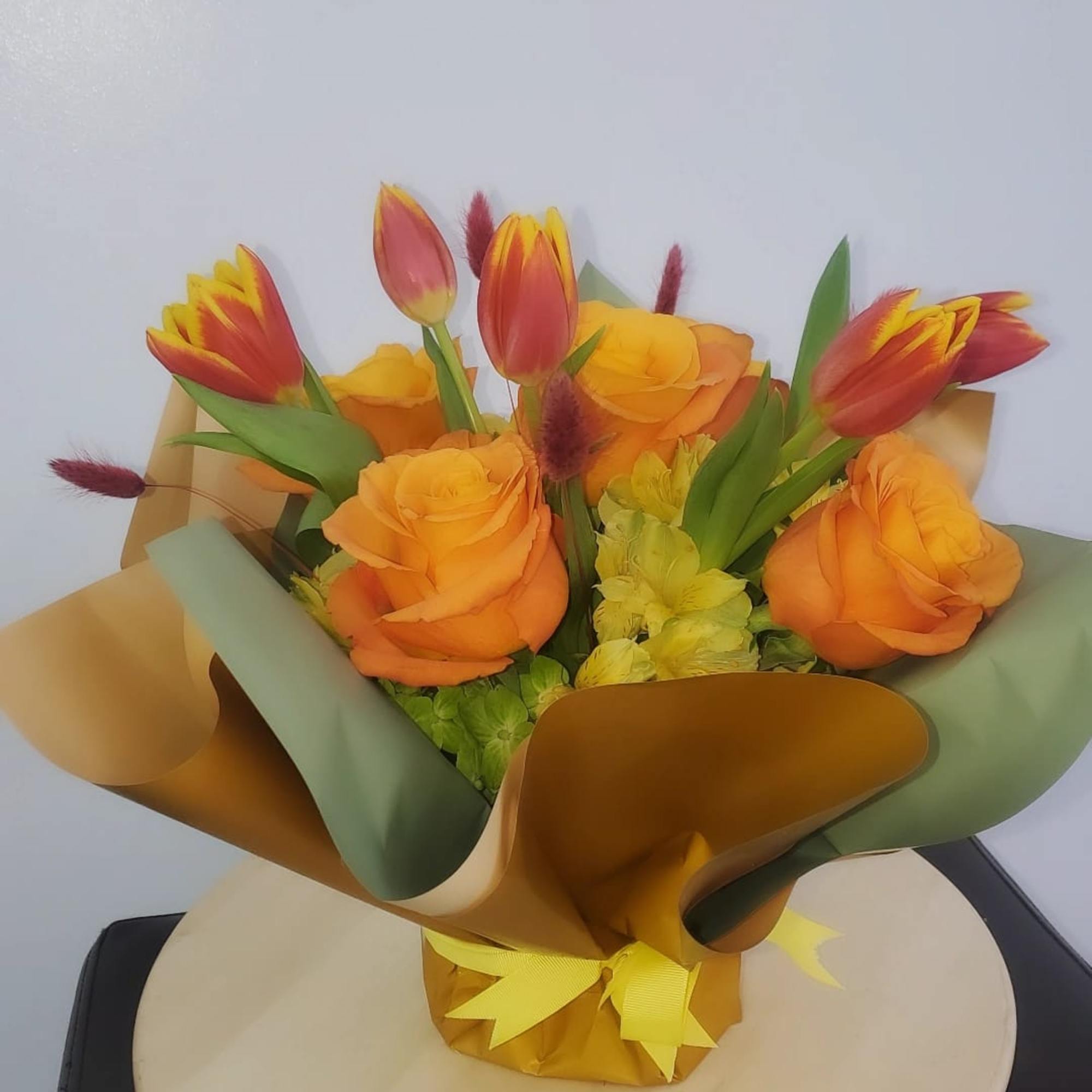 Bouquet of orange roses and red-yellow tulips wrapped in gold and green paper