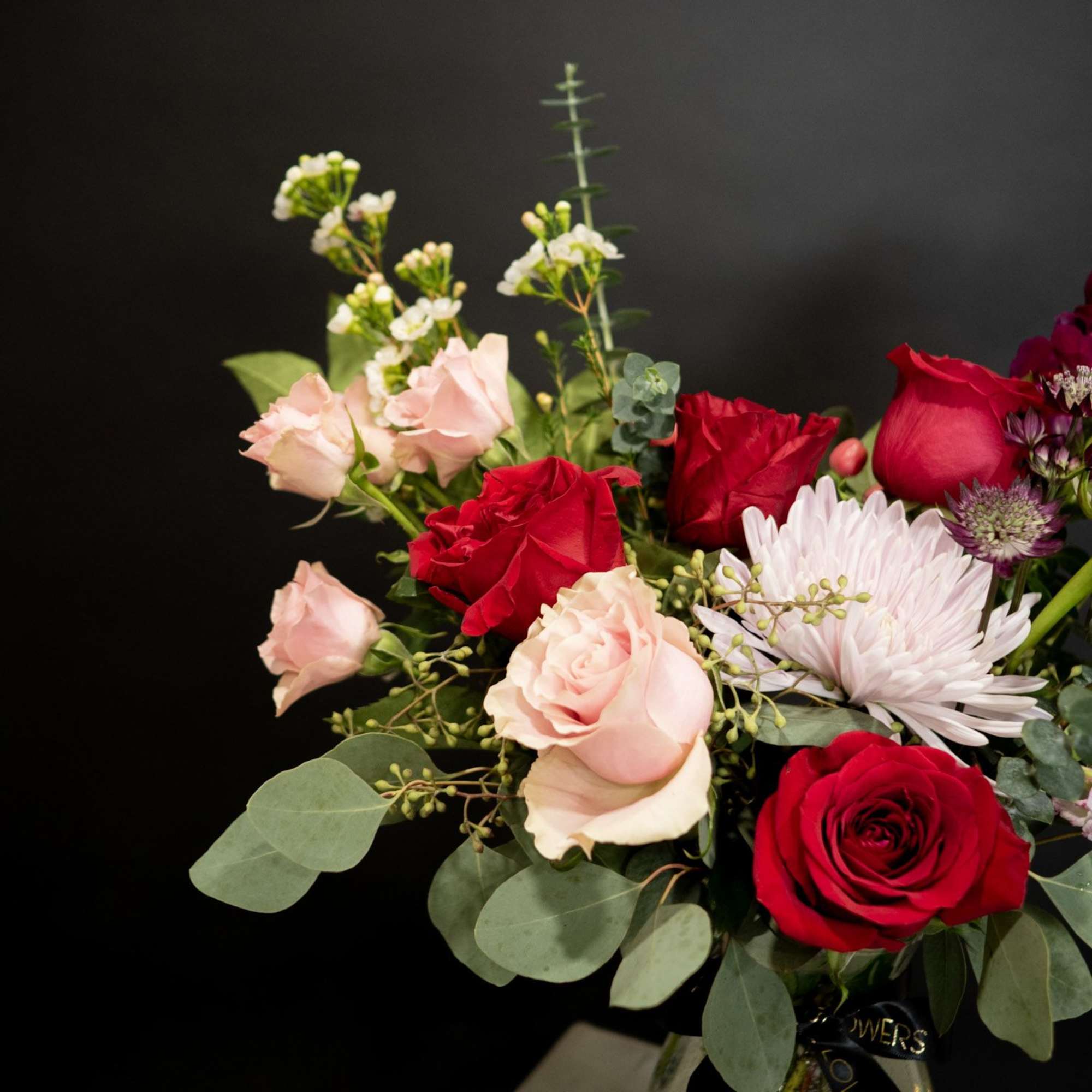 Bouquet of red and blush roses with a pale chrysanthemum in a glass vase