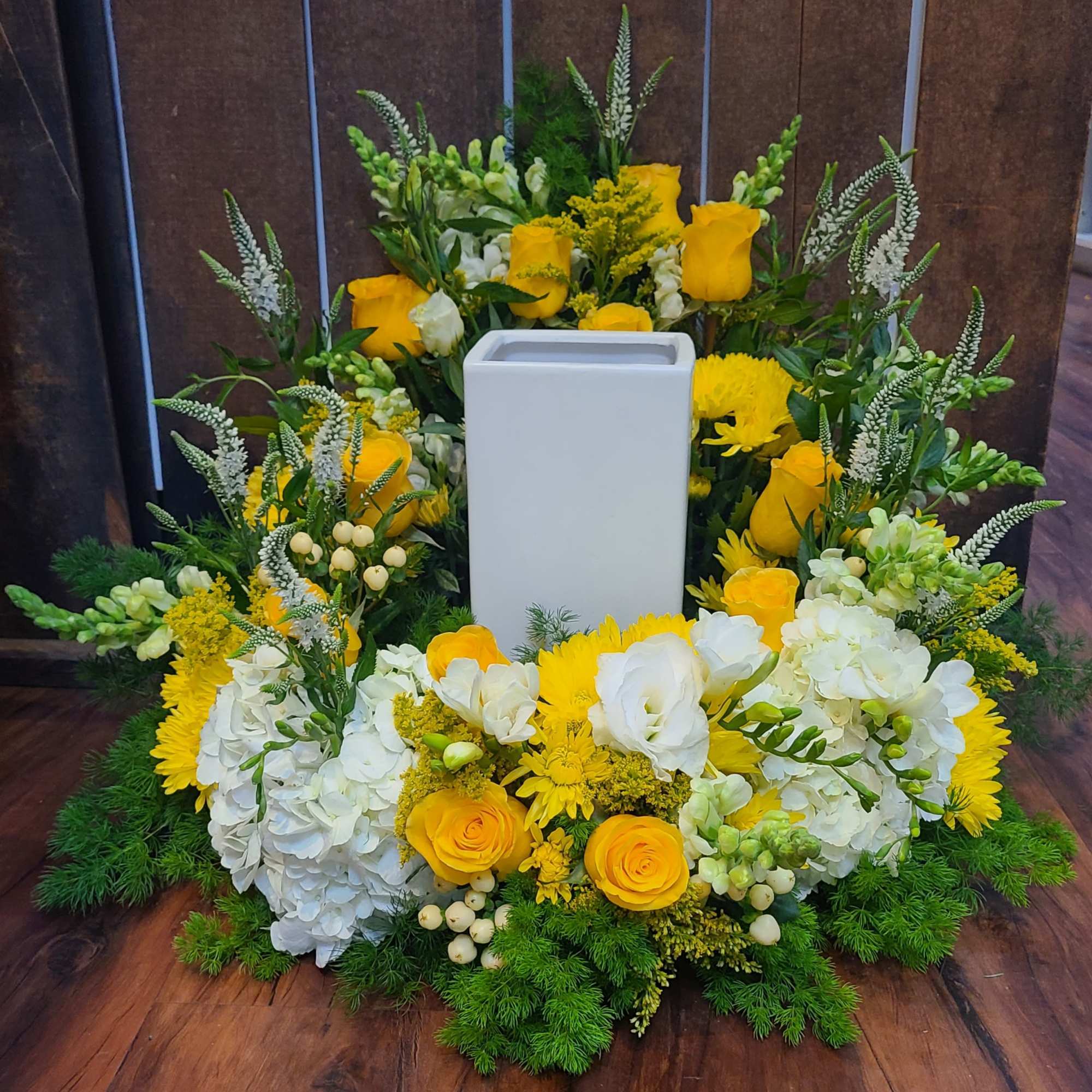 Yellow and white floral ring arrangement encircling a tall white rectangular vase