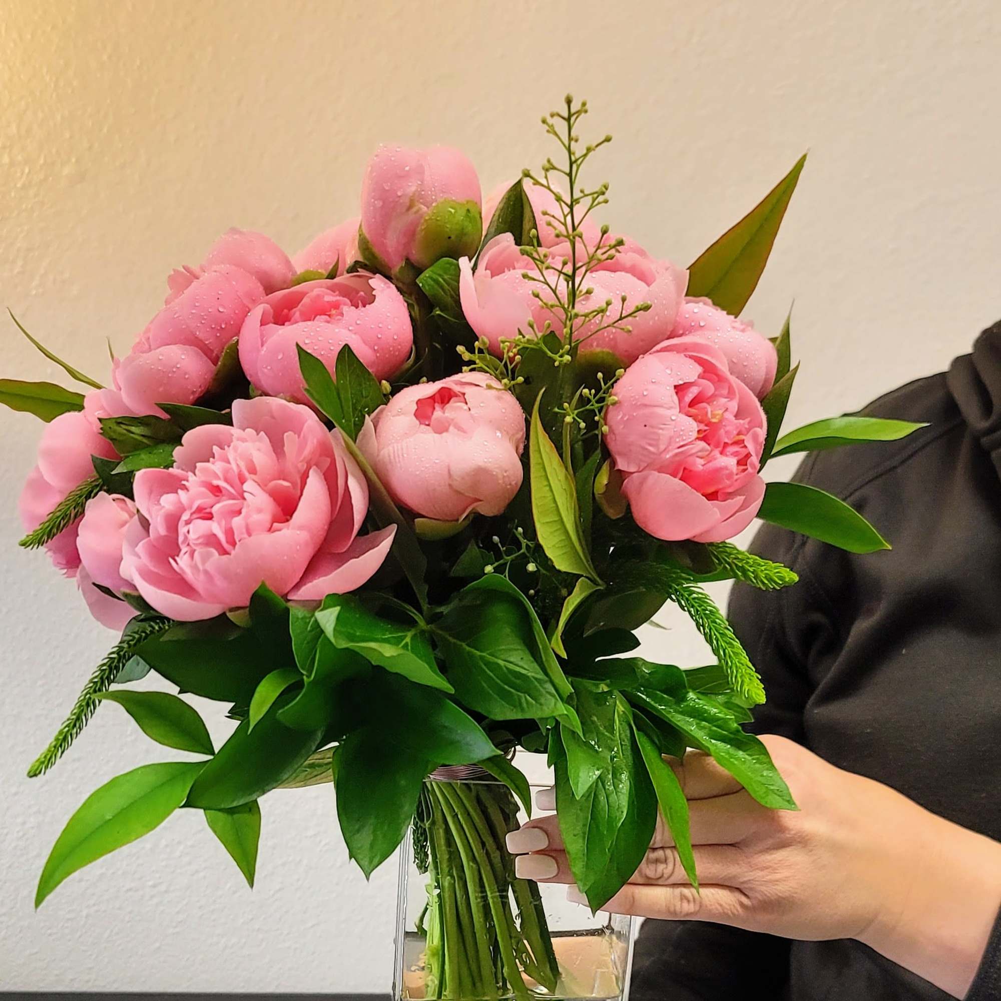 Pink peony bouquet with green foliage in a clear vase