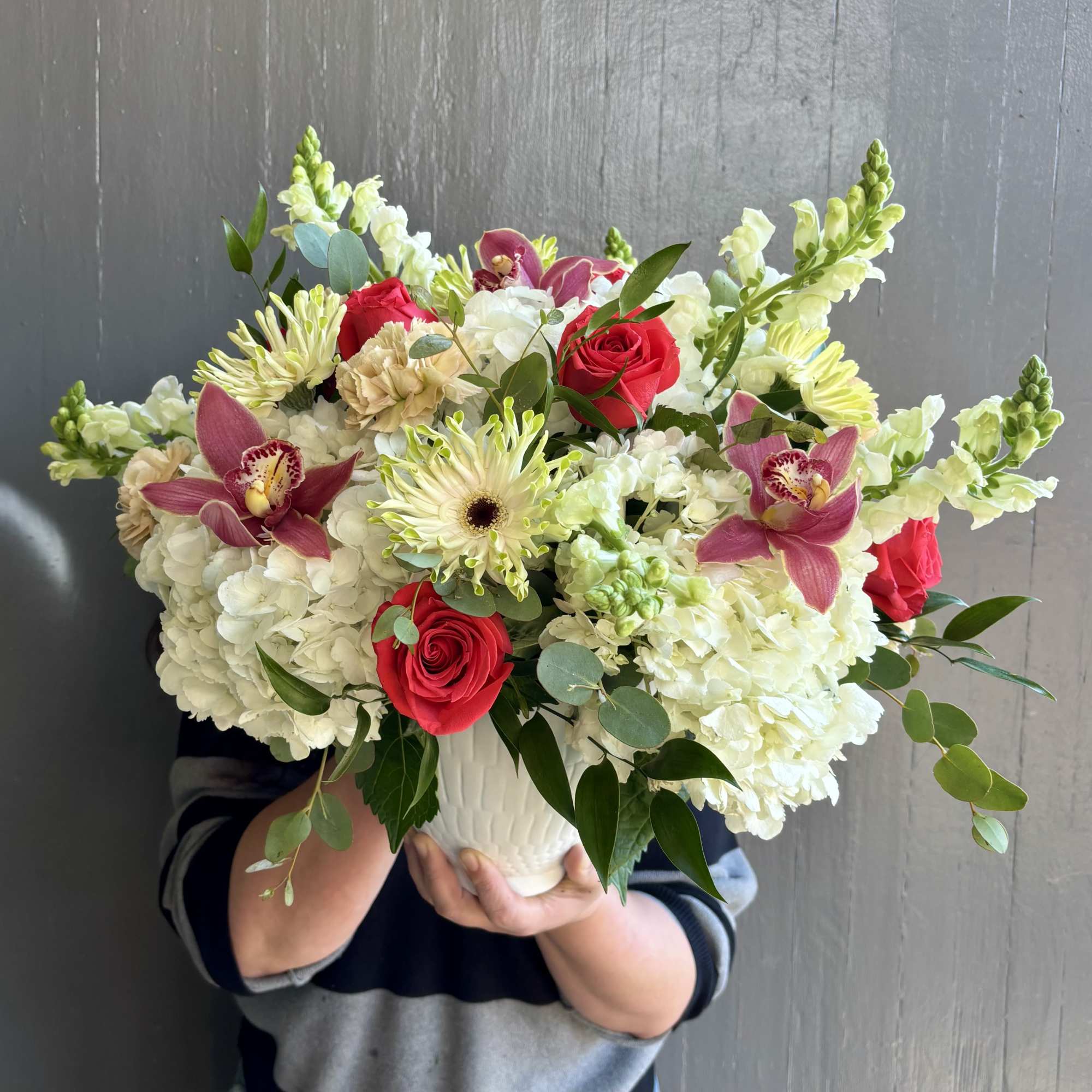 Bouquet of white hydrangeas, red roses, and pink orchids in a white vase
