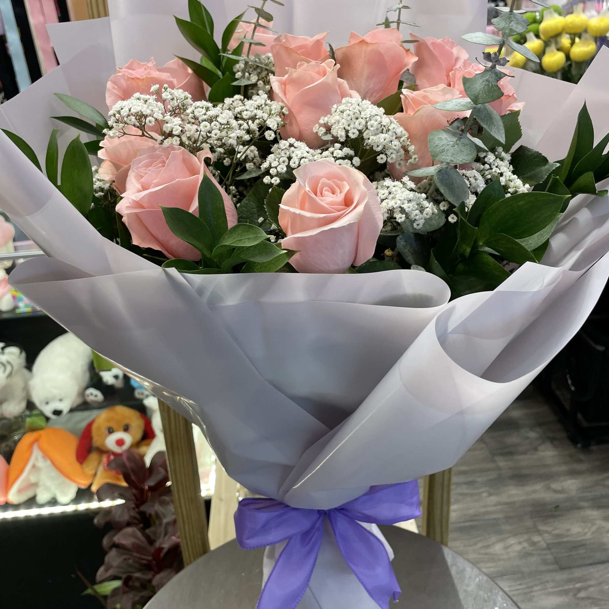 Bouquet of pink roses with white filler flowers and purple ribbon