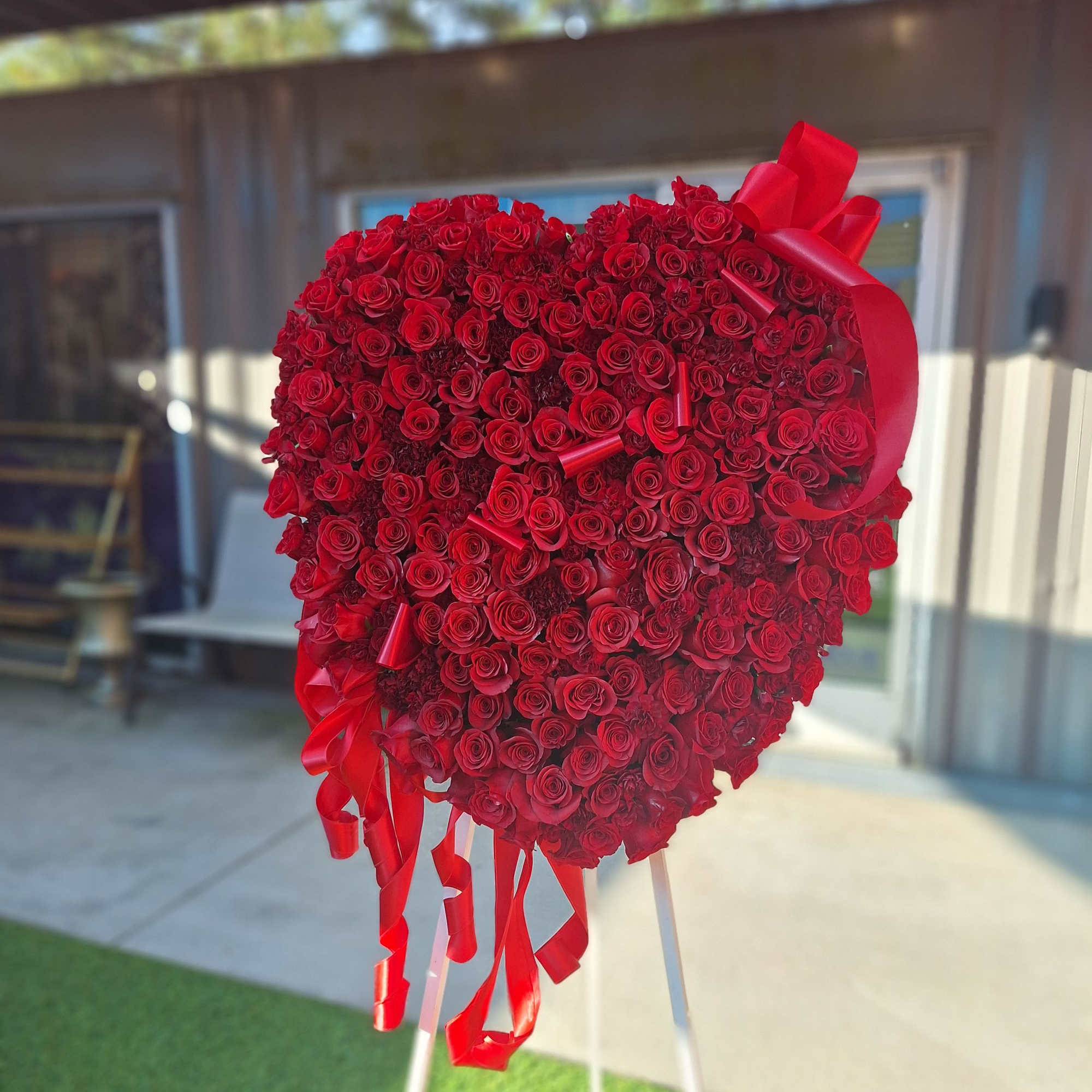 Heart-shaped red rose arrangement on a stand with ribbon streamers