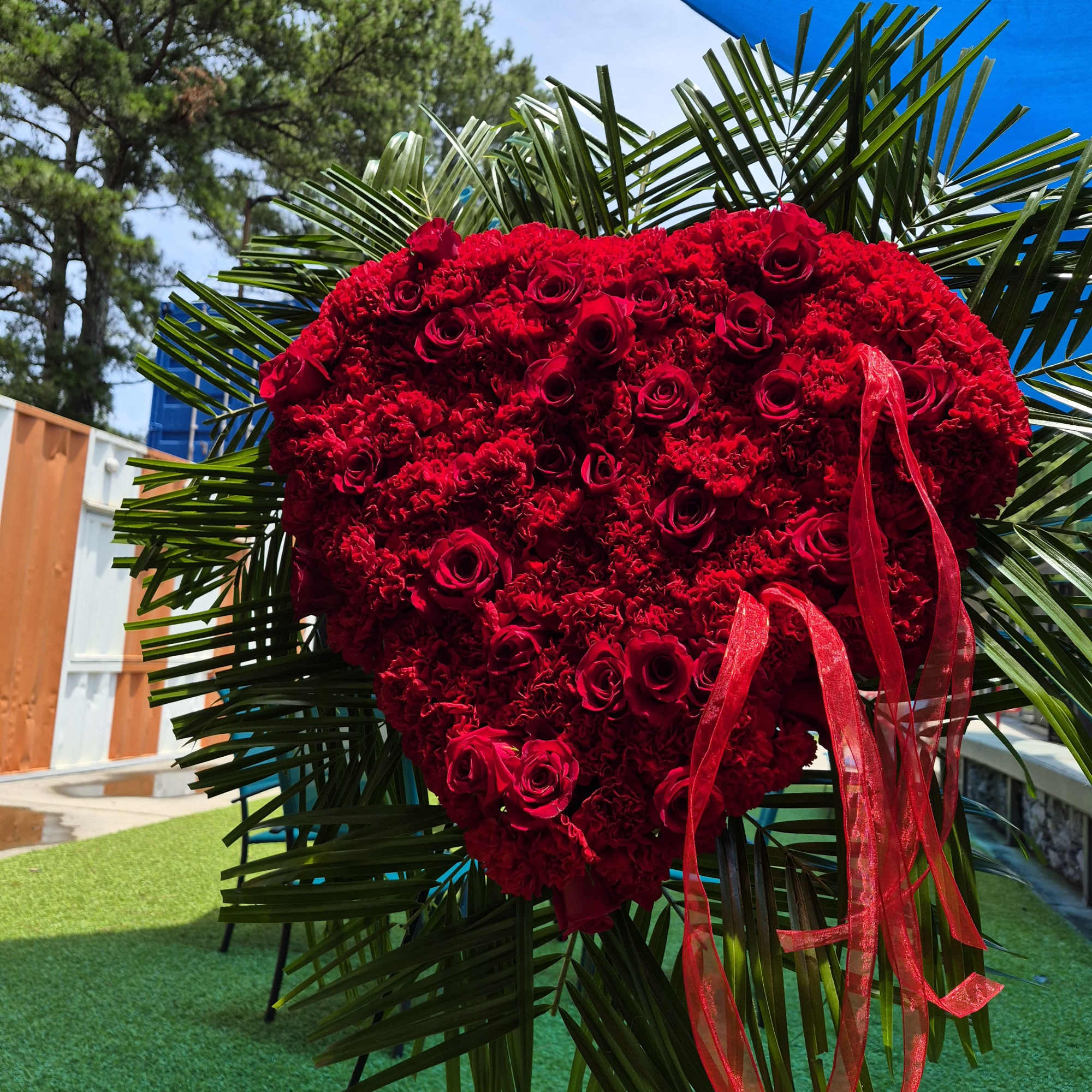 A closed heart wreath with red carnations and clusters of red roses
