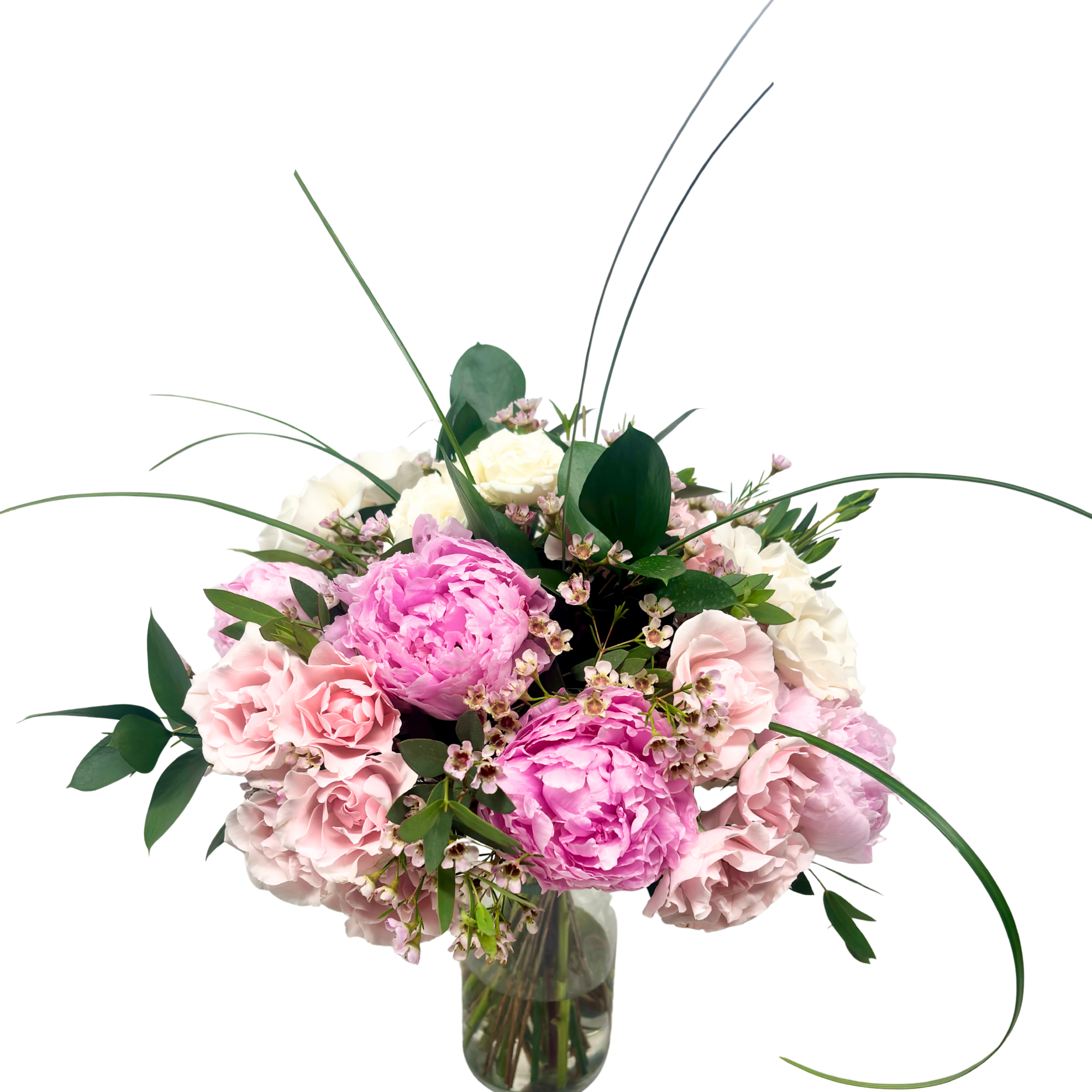 Pink and white peony and rose arrangement in a clear glass vase with looping grass accents
