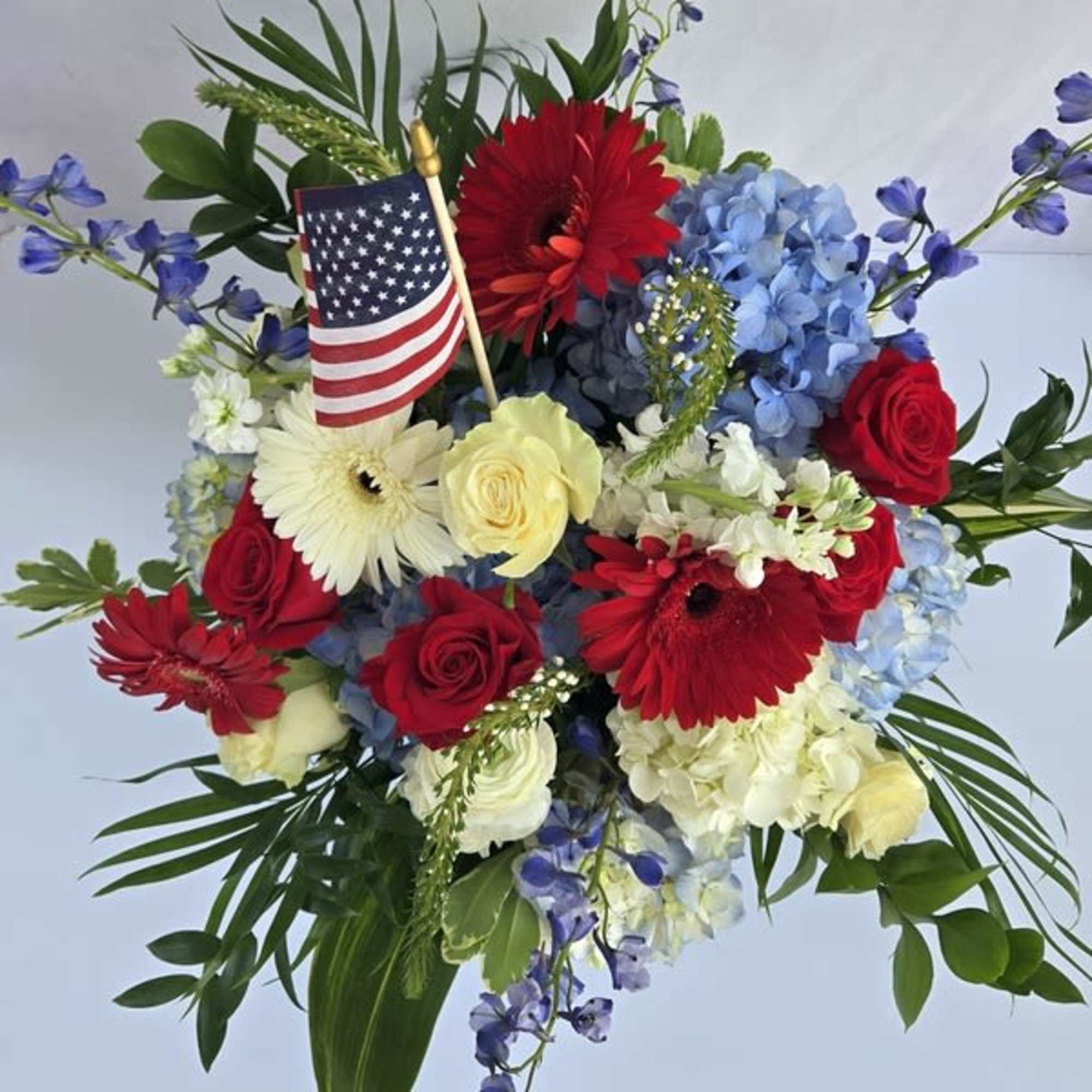 Patriotic red, white, and blue flower arrangement with roses, gerberas, hydrangeas, and a small US flag