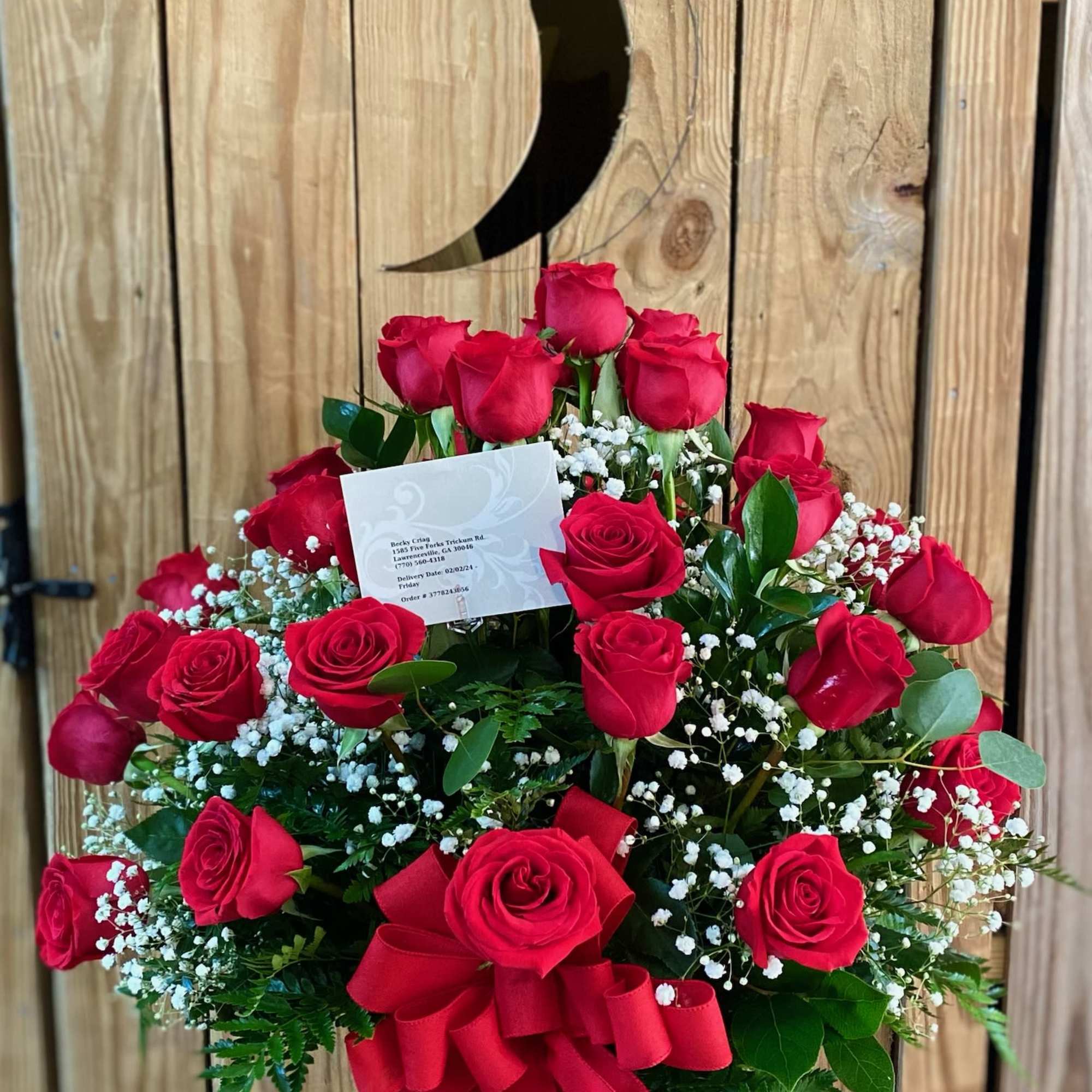 Arrangement of red roses with white filler flowers in a clear vase with a large red bow.