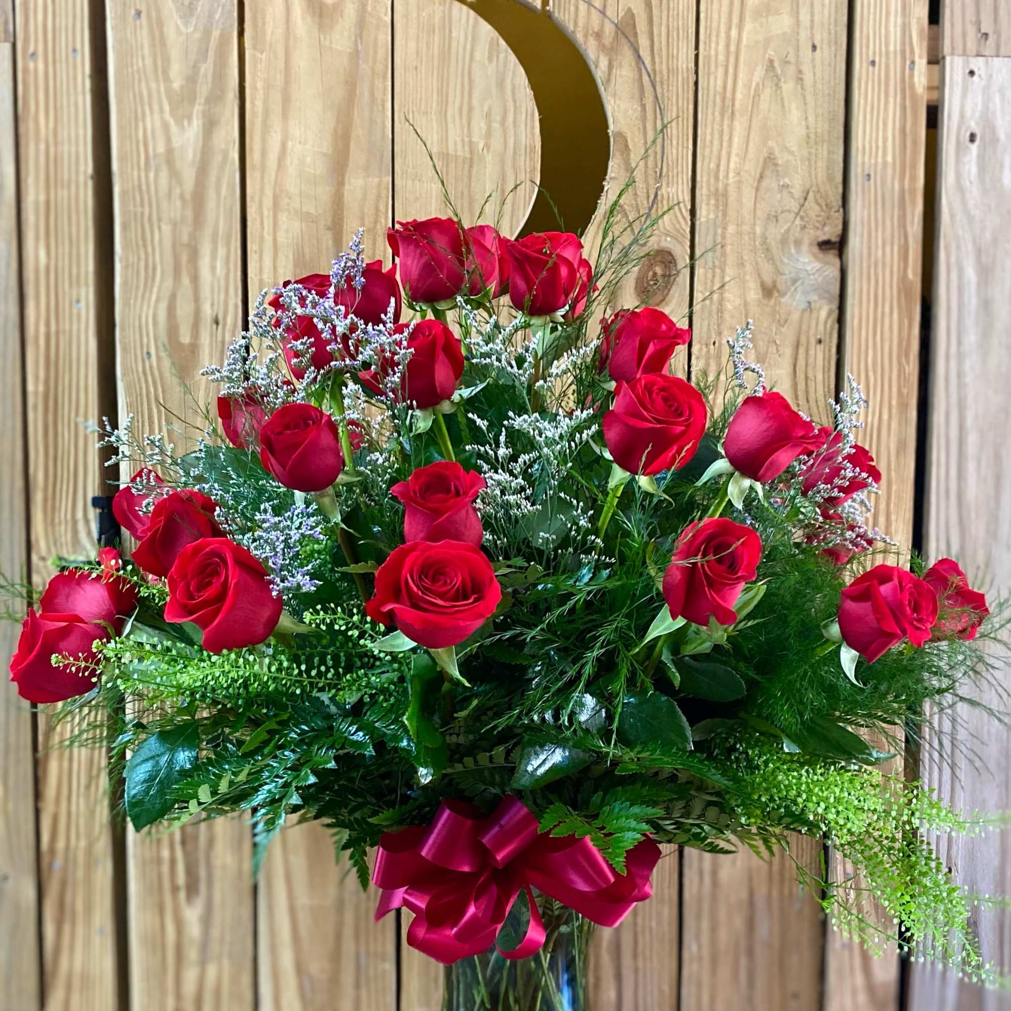 Tall arrangement of red roses with white filler flowers in a clear glass vase with a red bow.