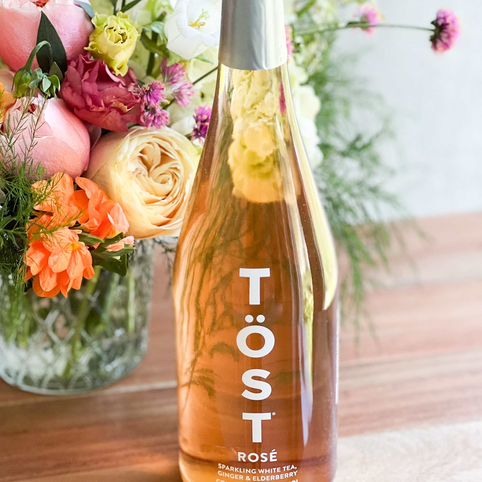 Bottle of rosé sparkling tea beside a pastel flower arrangement