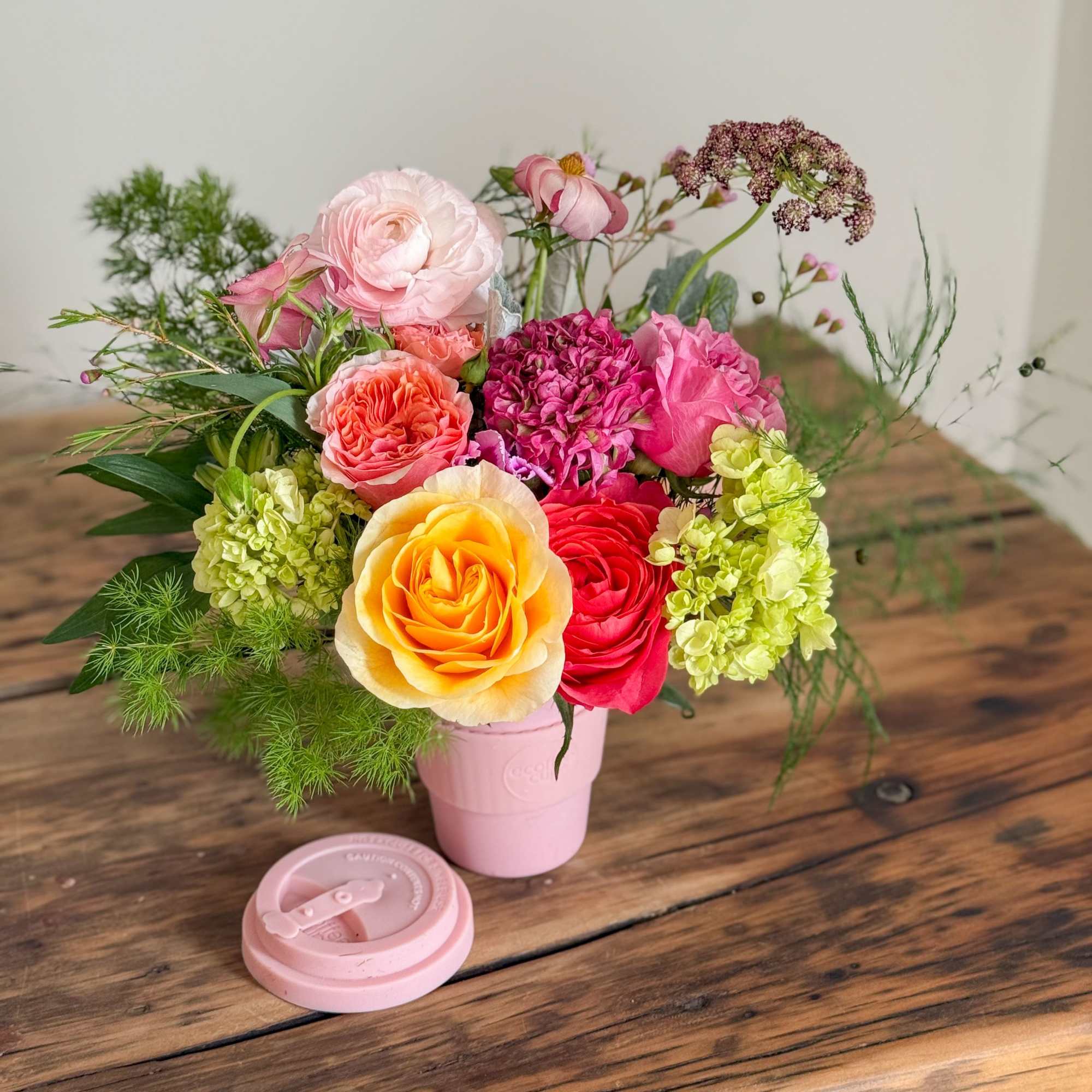 Mixed bouquet of roses and hydrangeas in a pink cup-style vase