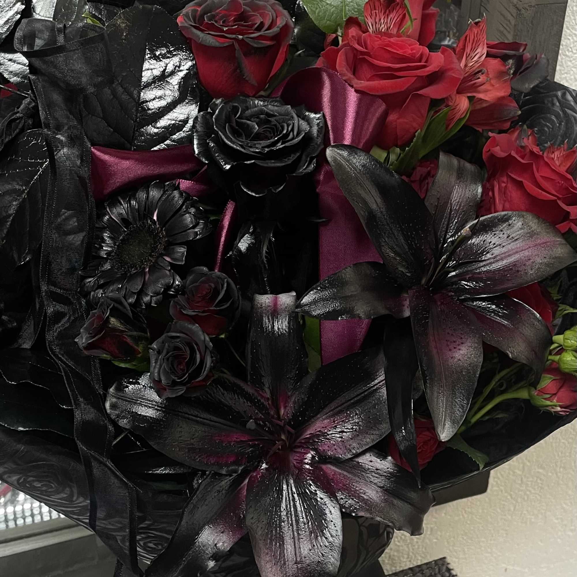 Bouquet of red and black roses with dark lilies in a glass vase