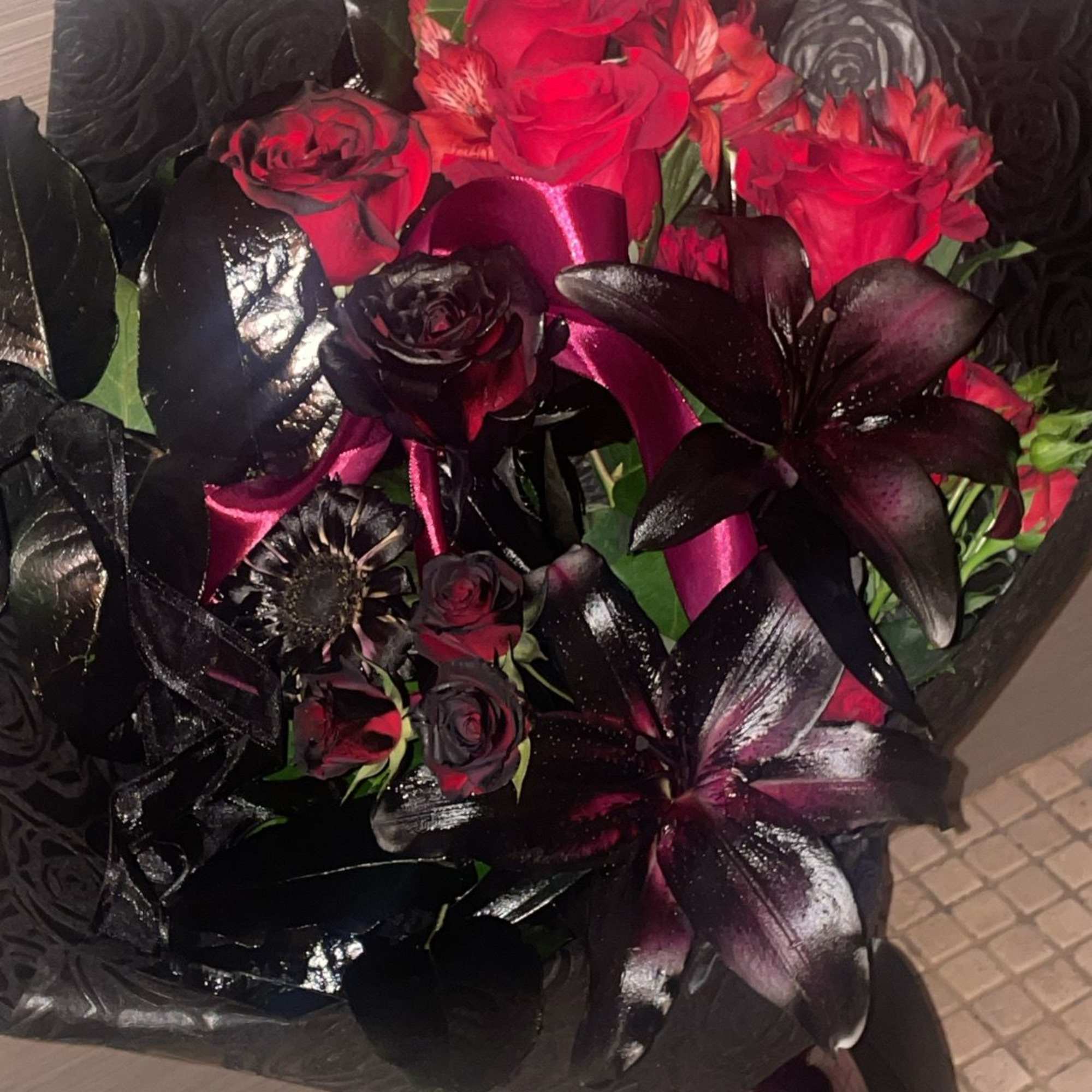 Bouquet of red roses and dark lilies wrapped in black paper