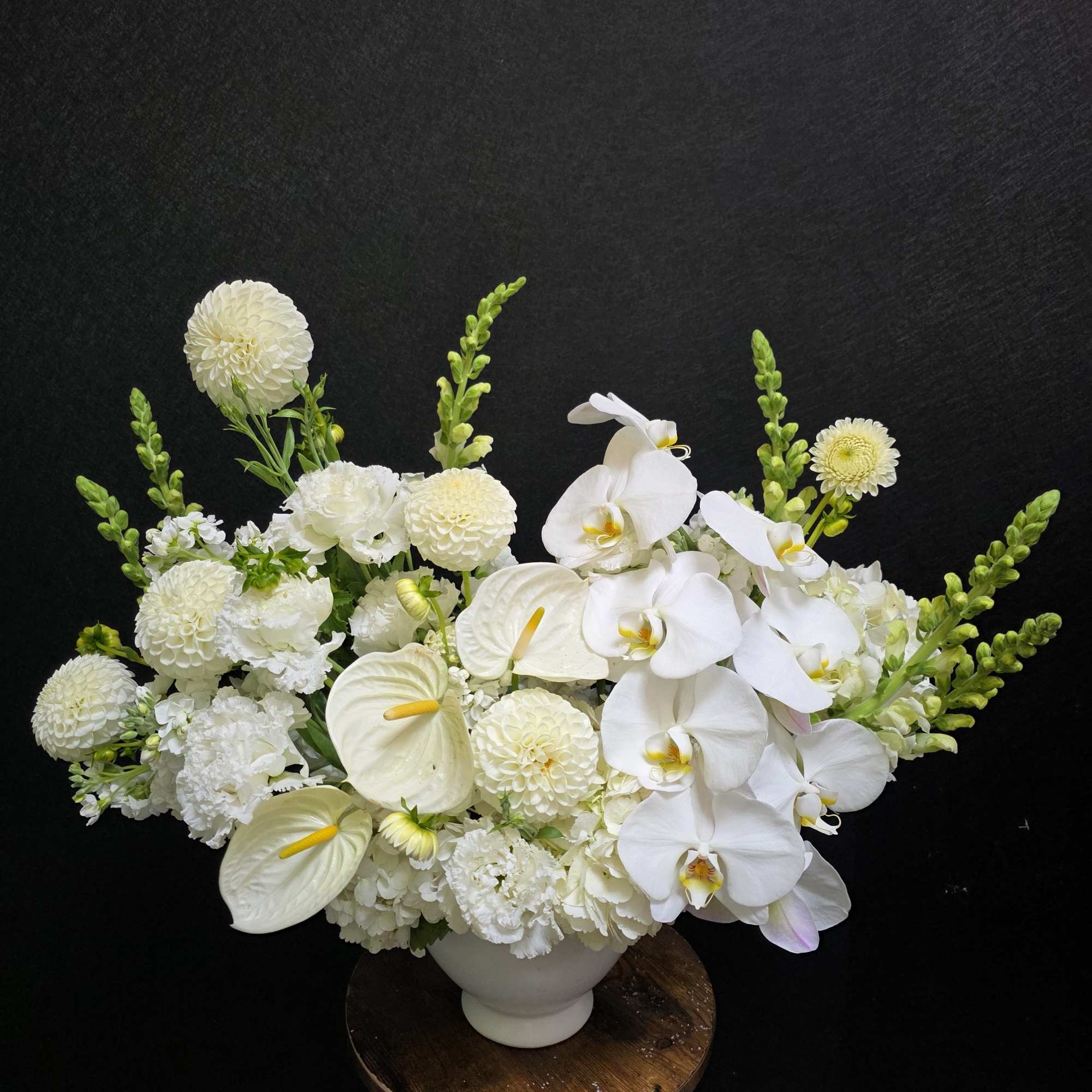 A serene low centerpiece of white phalaenopsis orchids, calla lilies, and anthuriums