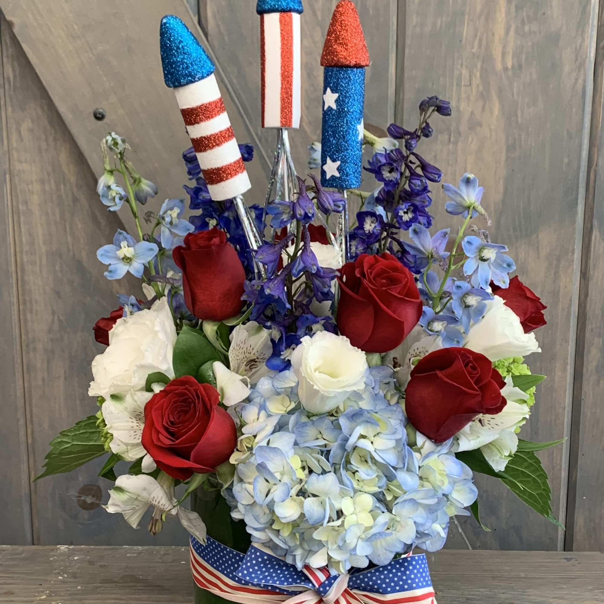 Red roses and blue hydrangeas in a glass vase with patriotic rocket picks