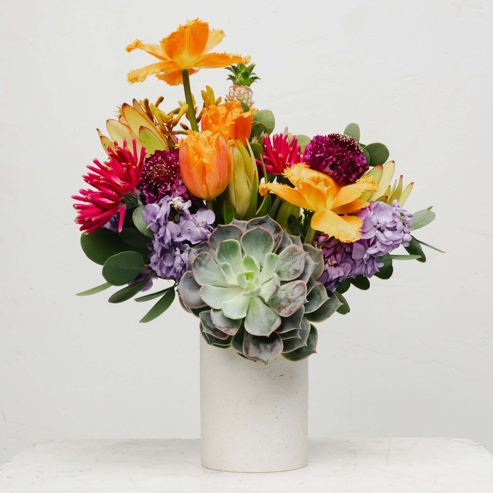 Colorful bouquet with succulents, orange tulips, and purple blooms in a white vase