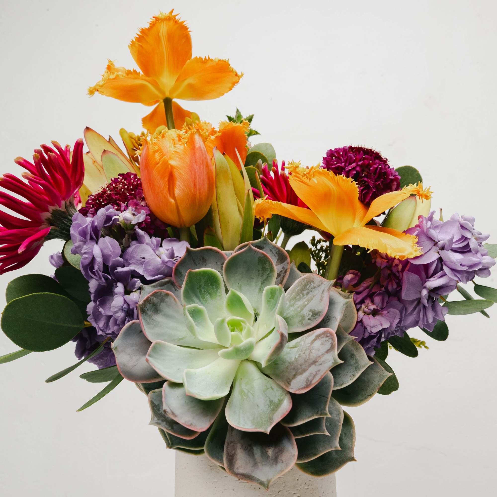 Bouquet with orange tulips, purple flowers, and a large succulent in a vase