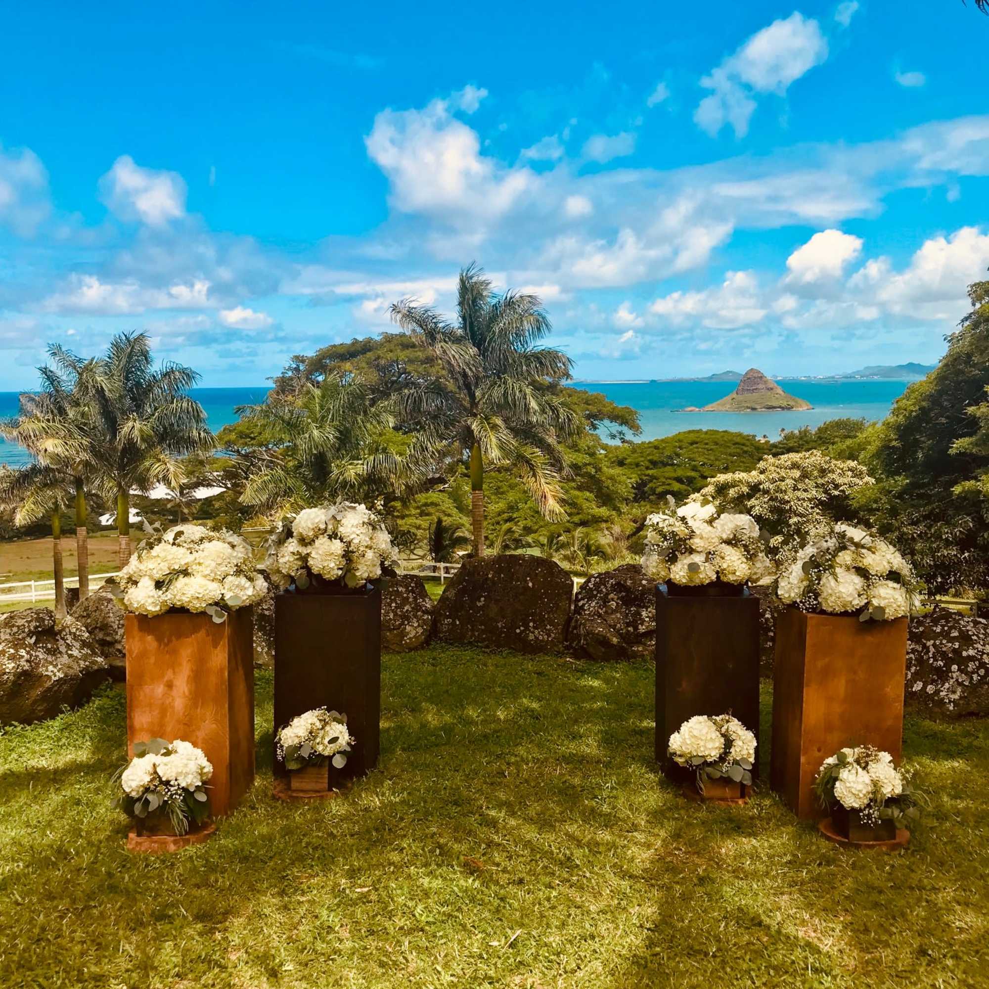 White floral arrangements on tall pedestals in an outdoor seaside setting