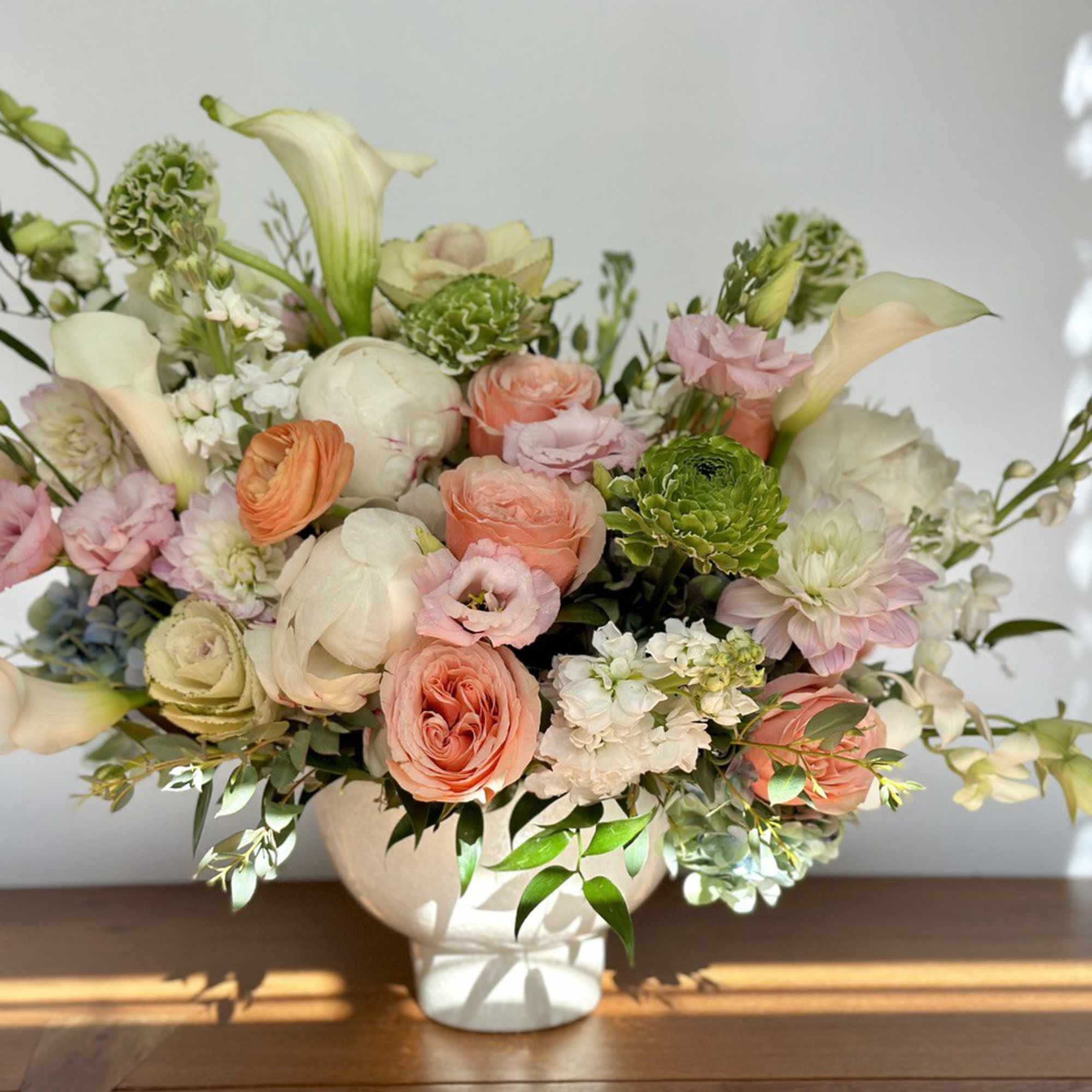 Pastel floral arrangement in a white vase with roses and calla lilies