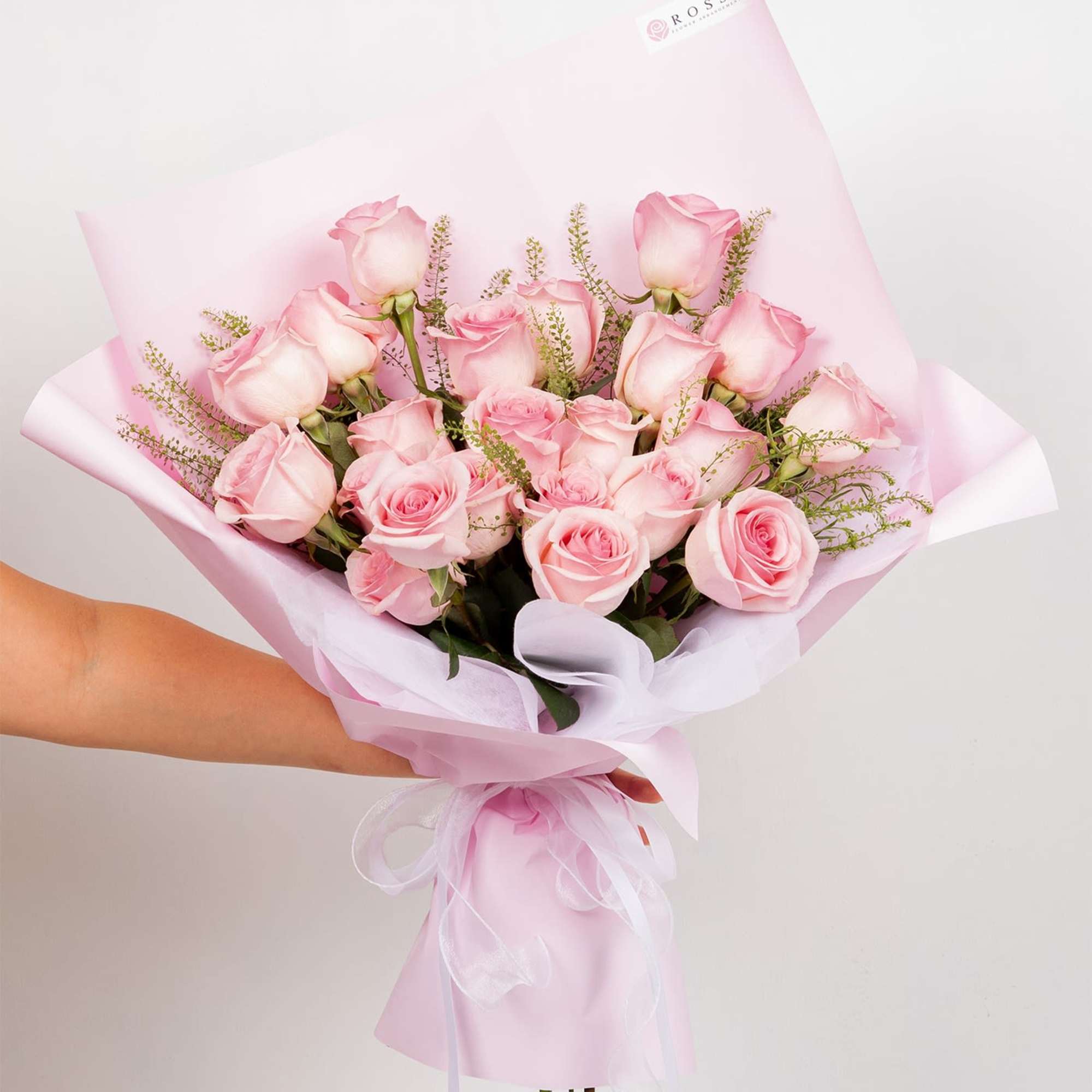 Handheld bouquet of pink roses wrapped in pale pink paper