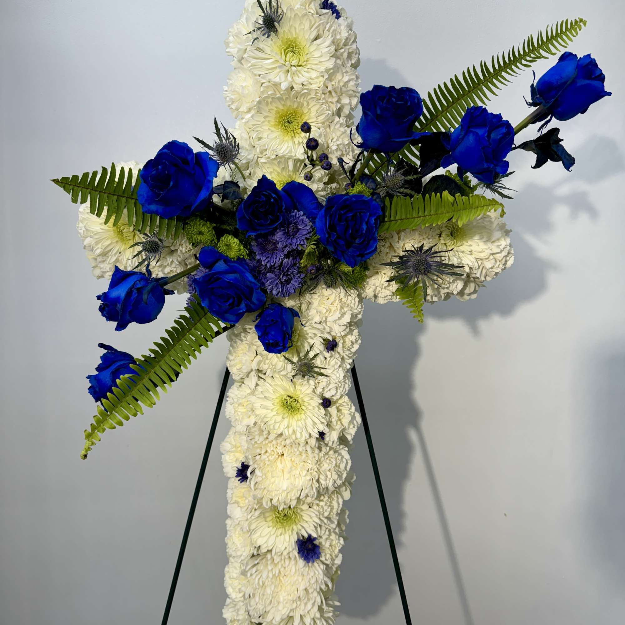 White floral cross on an easel with blue roses and fern accents