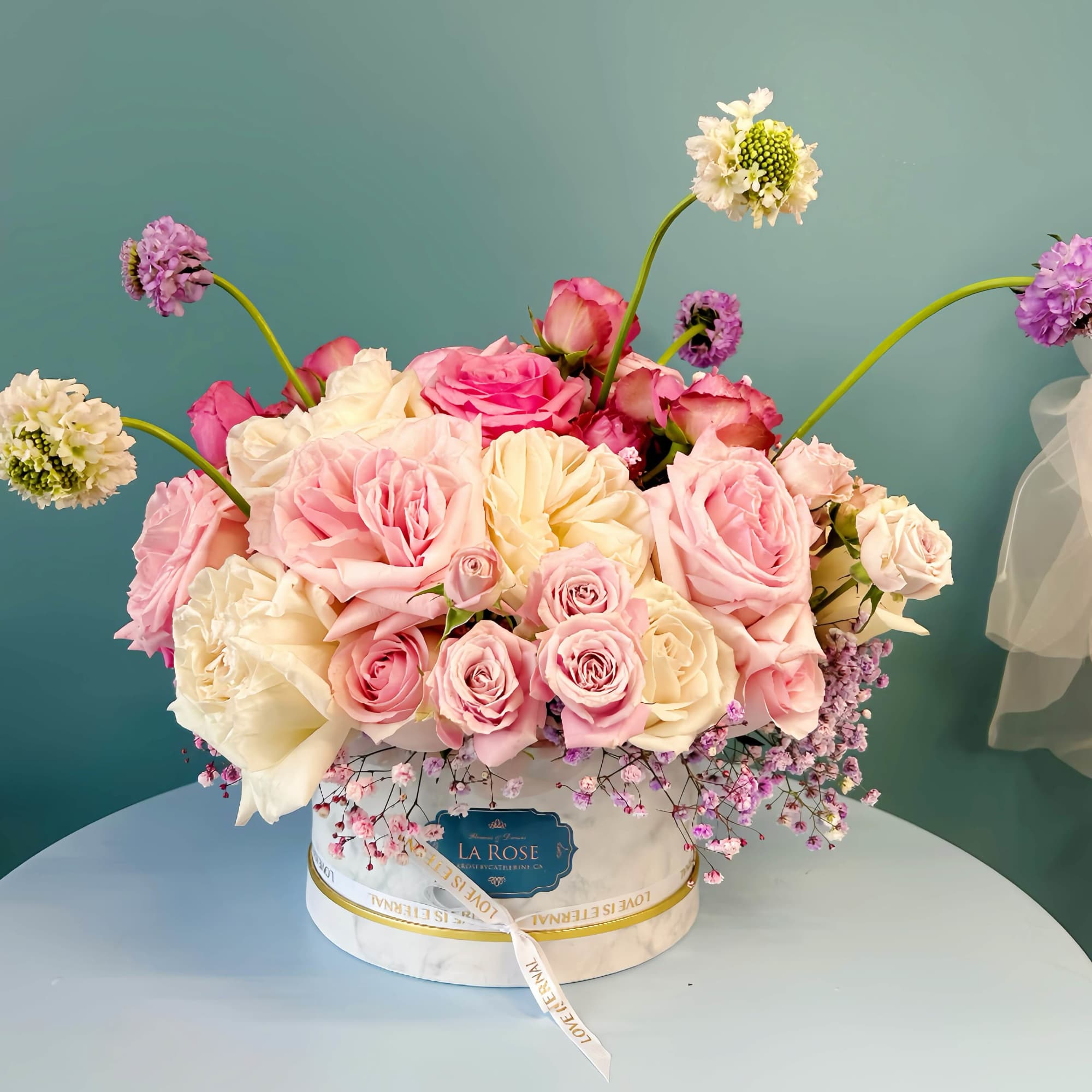 Pink and cream rose arrangement in a round box with small purple accents