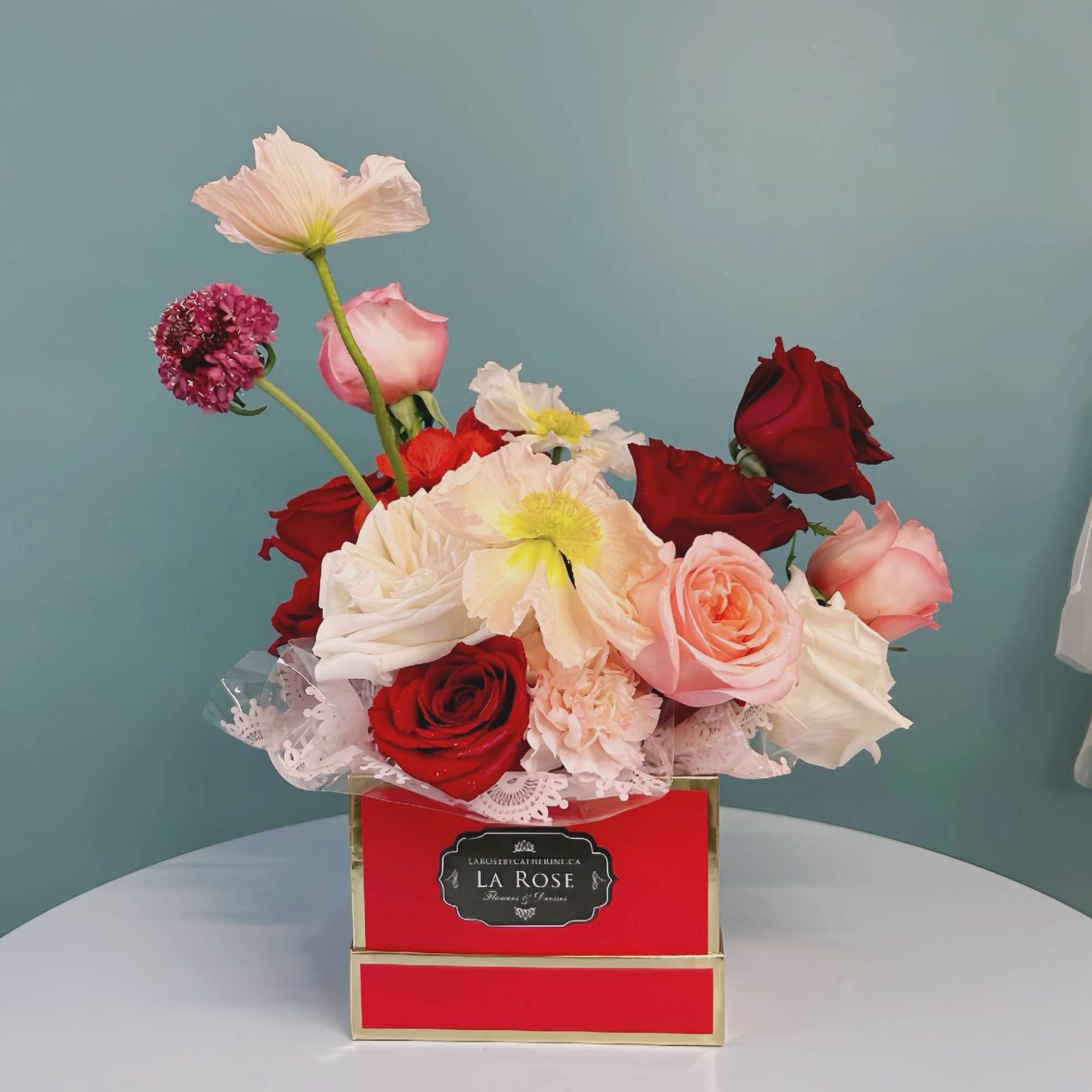 Red and pink roses arranged in a red box with white flowers