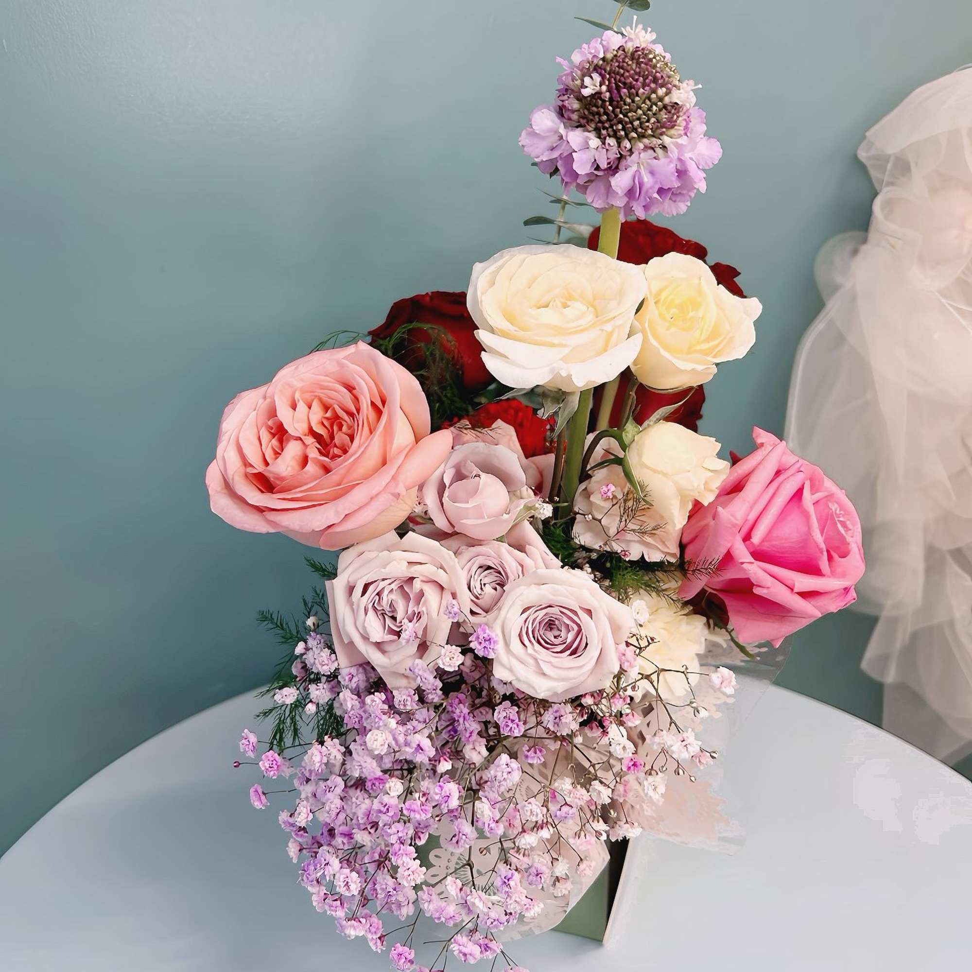 Tall bouquet of pink, white, and lavender roses with small purple filler flowers