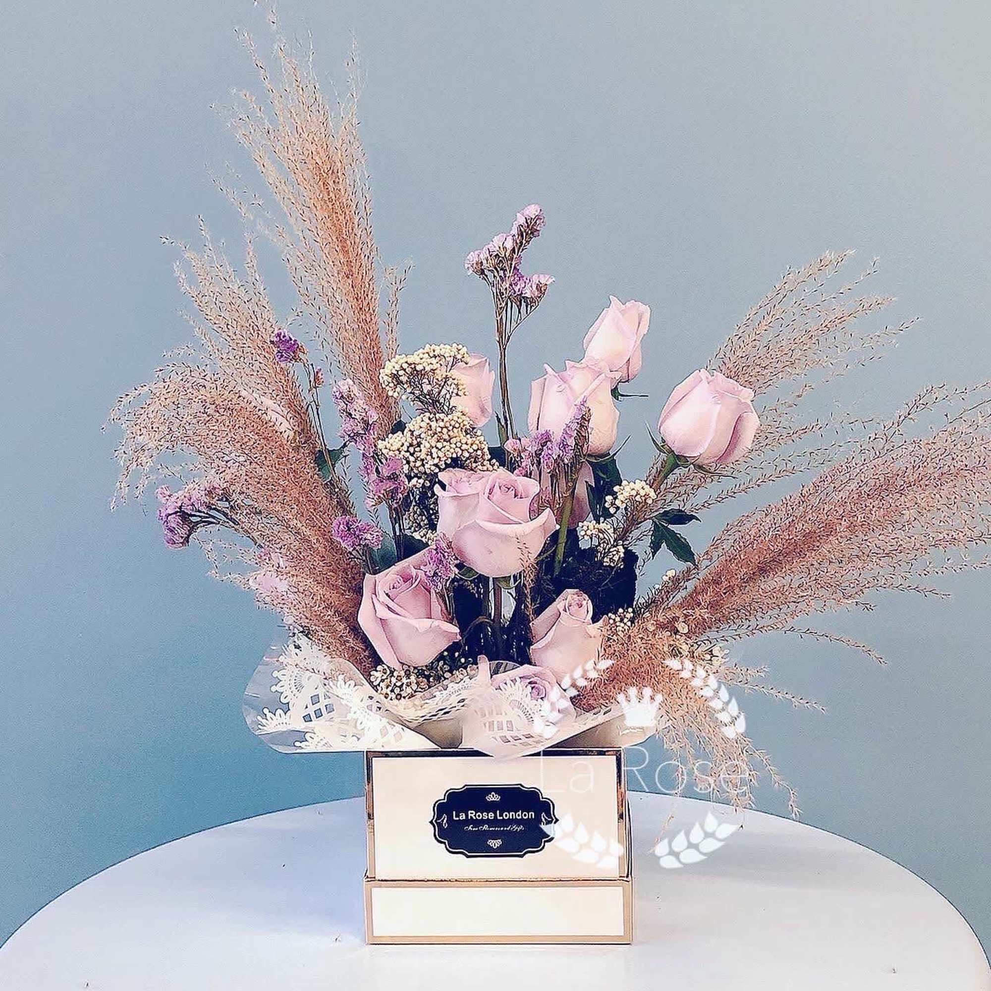 Pink roses arranged in a decorative box with airy dried plumes
