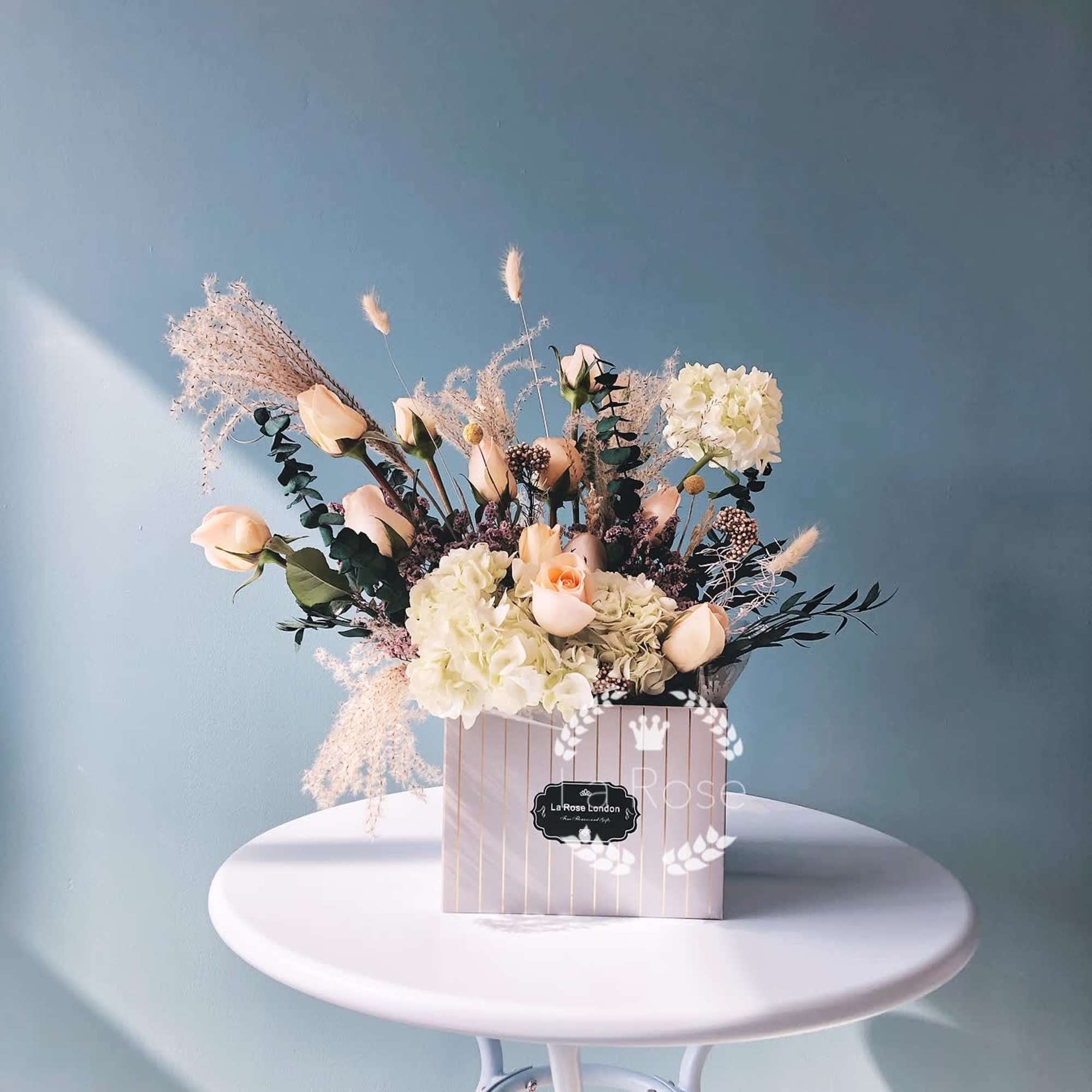 Blush roses and white hydrangeas arranged in a striped box