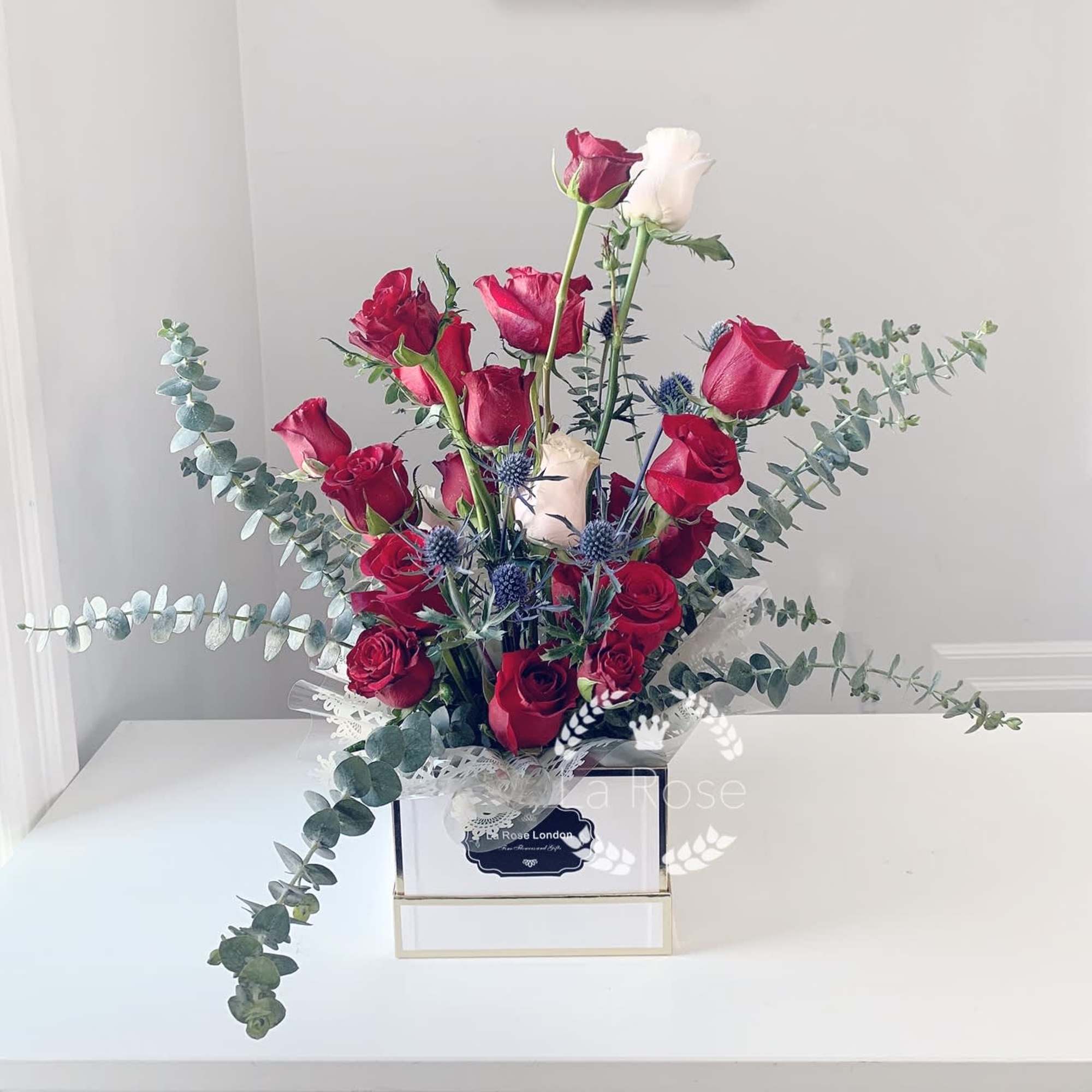 Red and white roses in a square box with eucalyptus and blue thistle