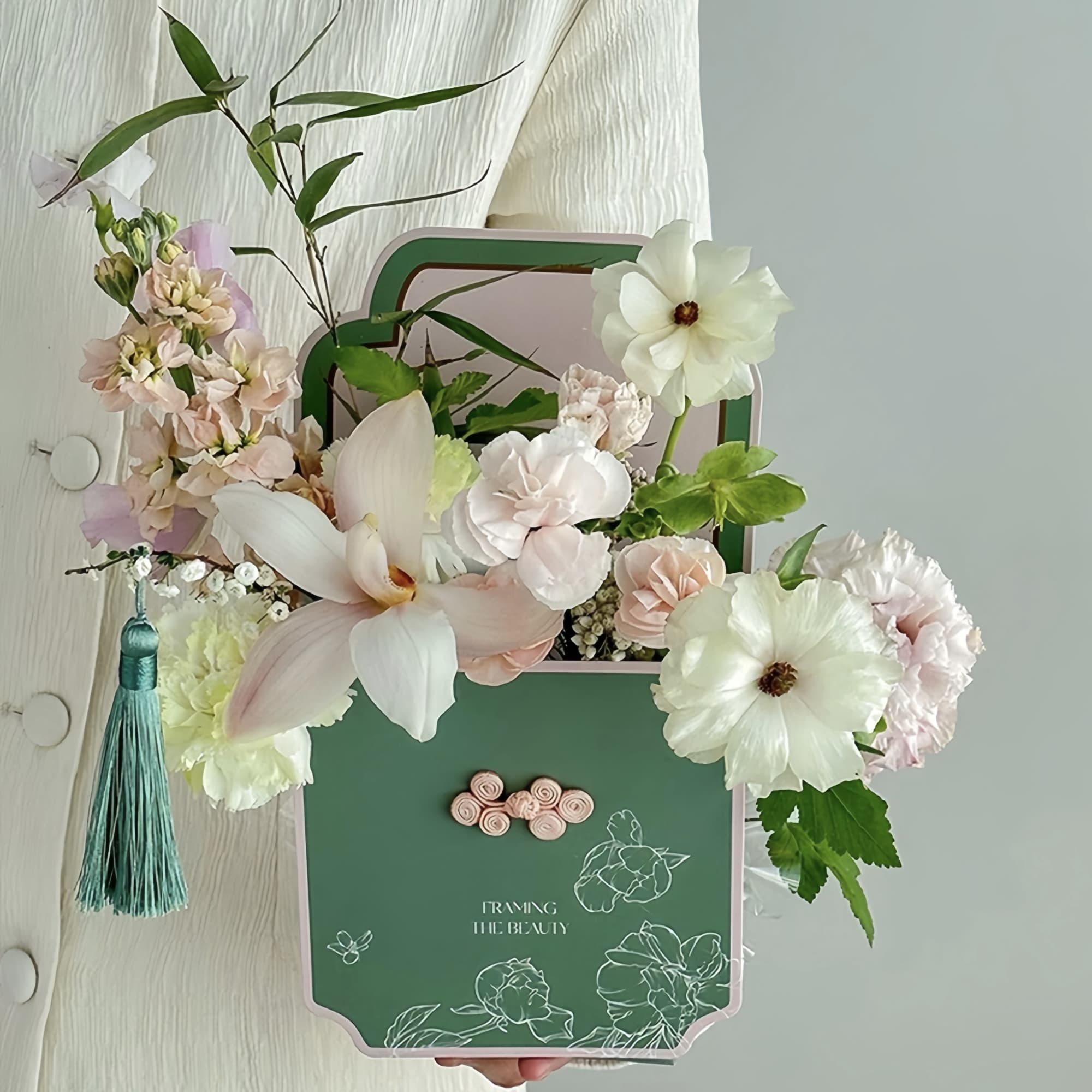 Pastel floral arrangement in a decorative green box with a tassel