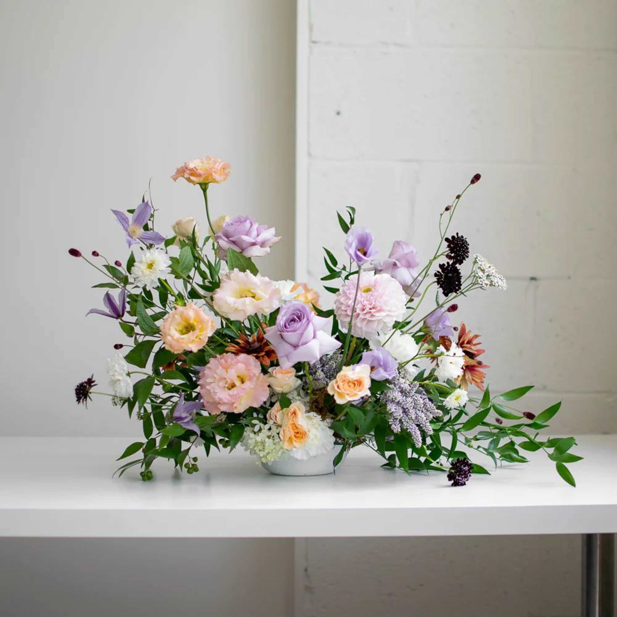 Low floral arrangement in a white bowl with pastel pink, lavender, and peach blooms