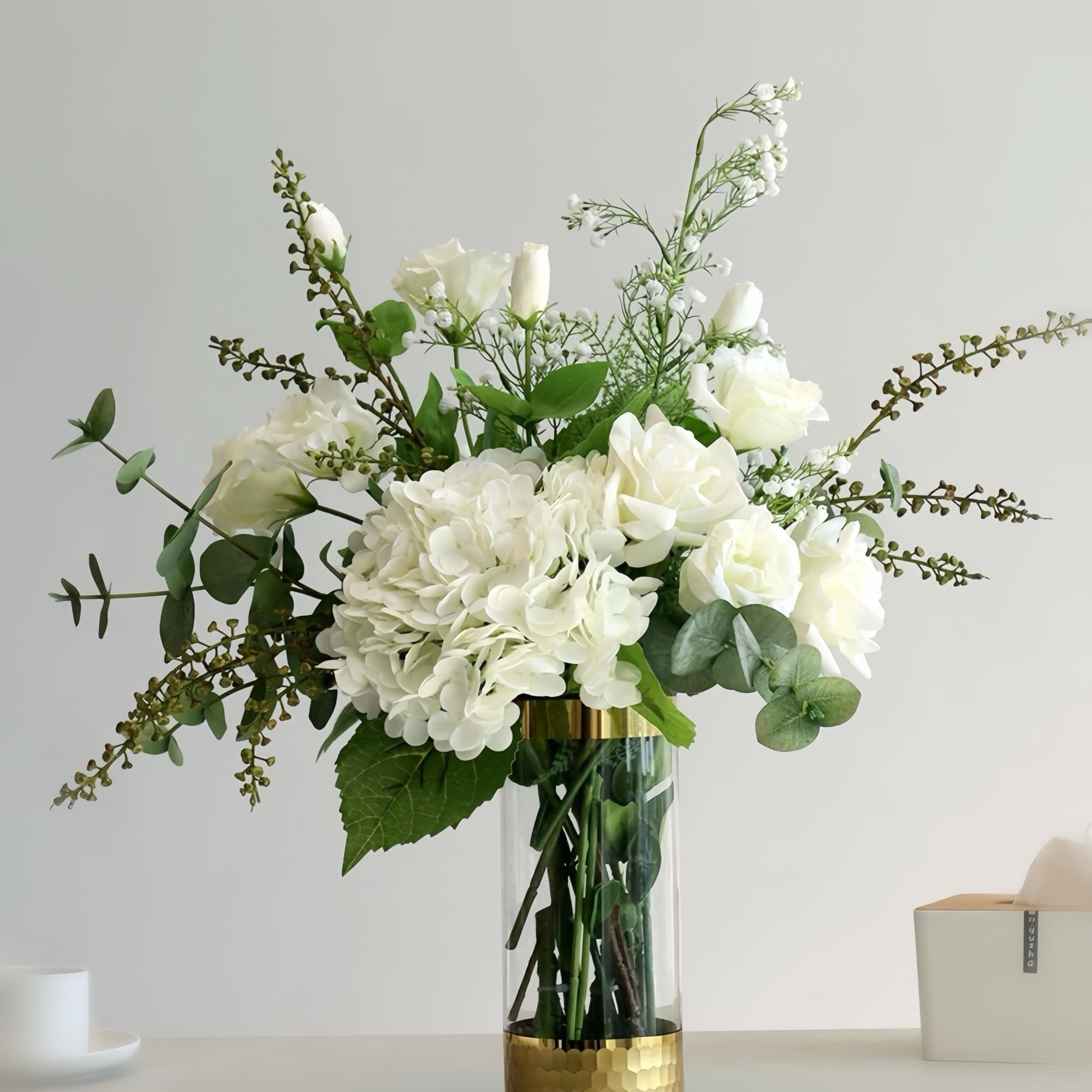 White roses and hydrangea in a glass vase with greenery
