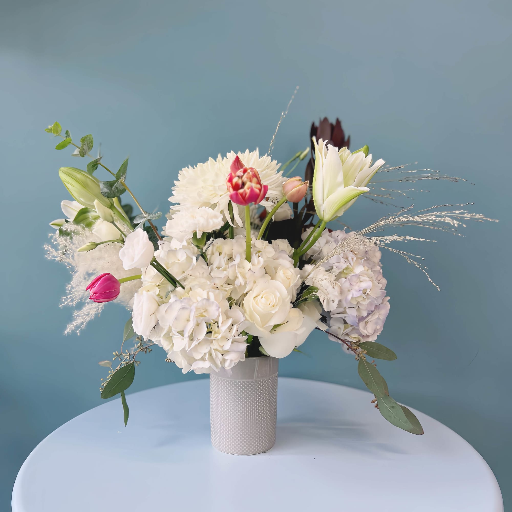 White floral arrangement with lilies, roses, and hydrangeas in a textured vase