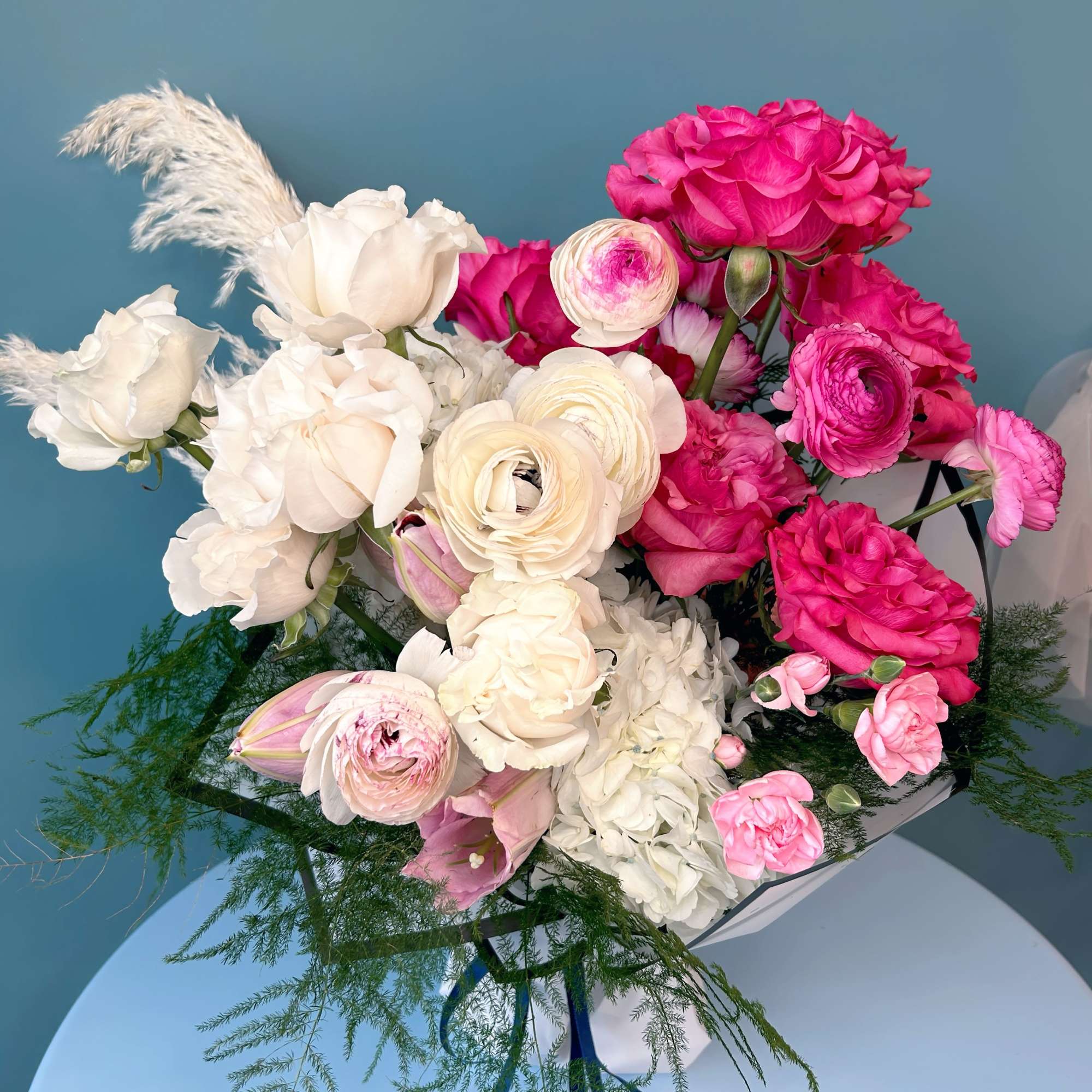 Bouquet of pink and white flowers with feathery greenery tied with blue ribbon