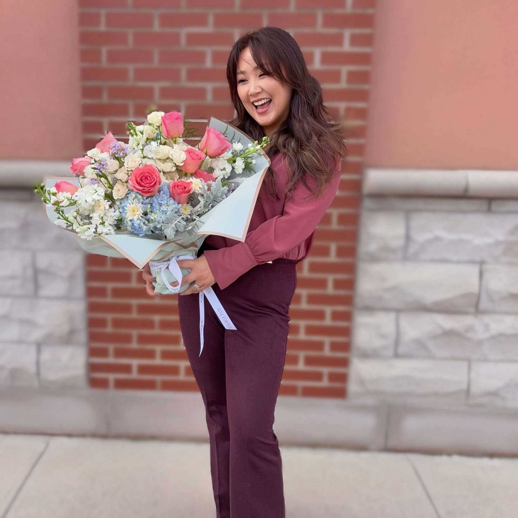Woman holding a large bouquet of pink and white flowers wrapped in pale paper