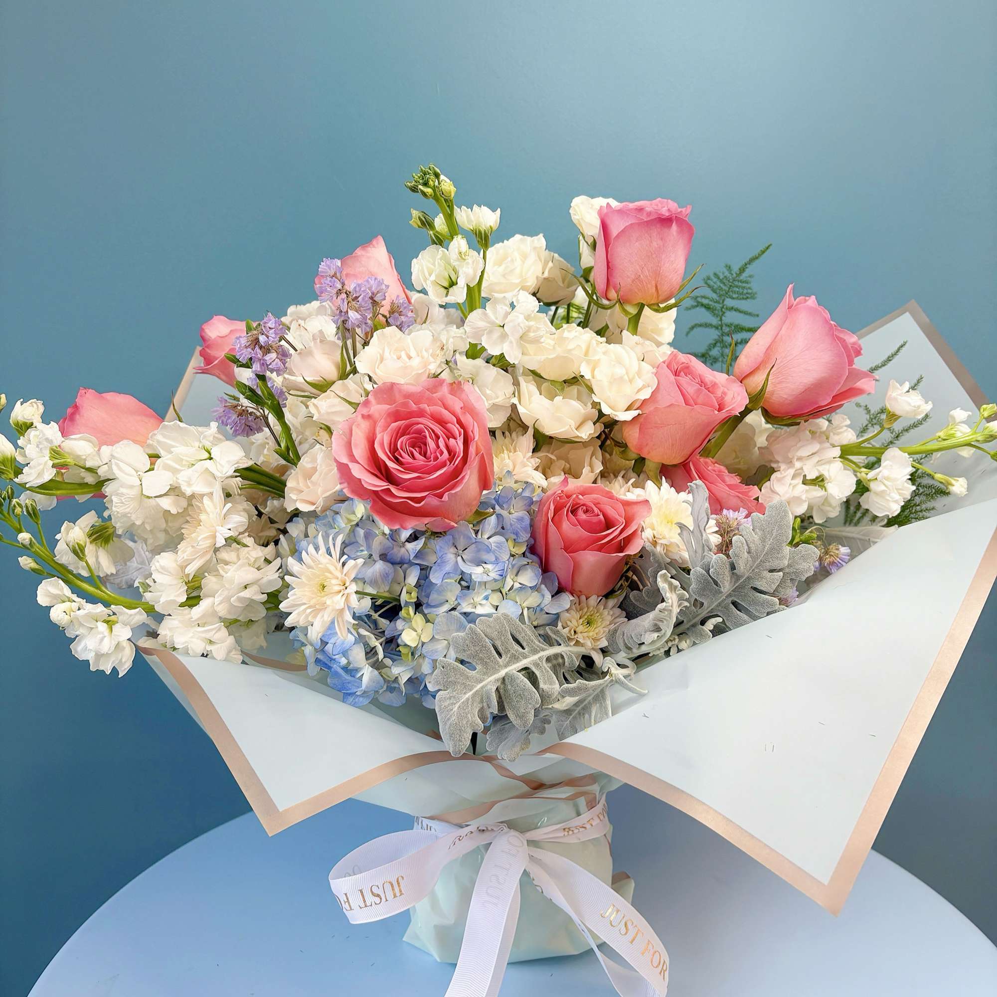 Bouquet of pink roses, white blooms, and blue hydrangea in pastel wrap