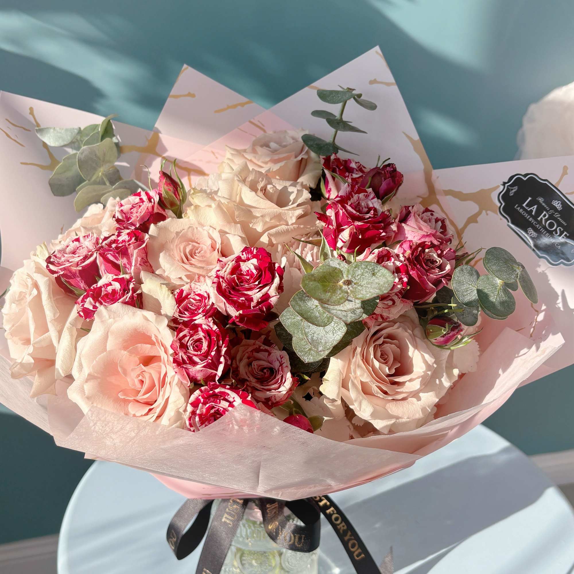 Bouquet of pale pink and red roses in pink wrap with a glass vase